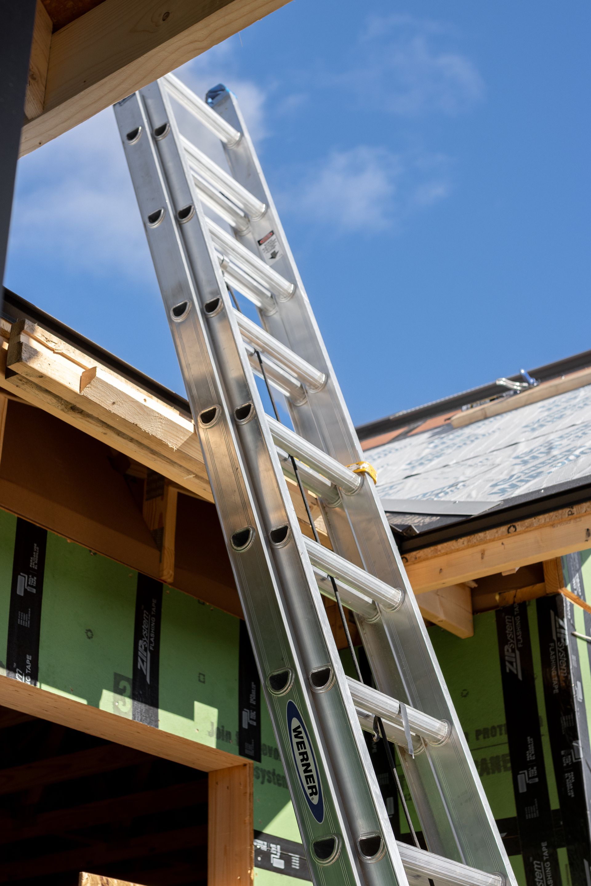 Ladder leaning against a building, reaching towards the blue sky.