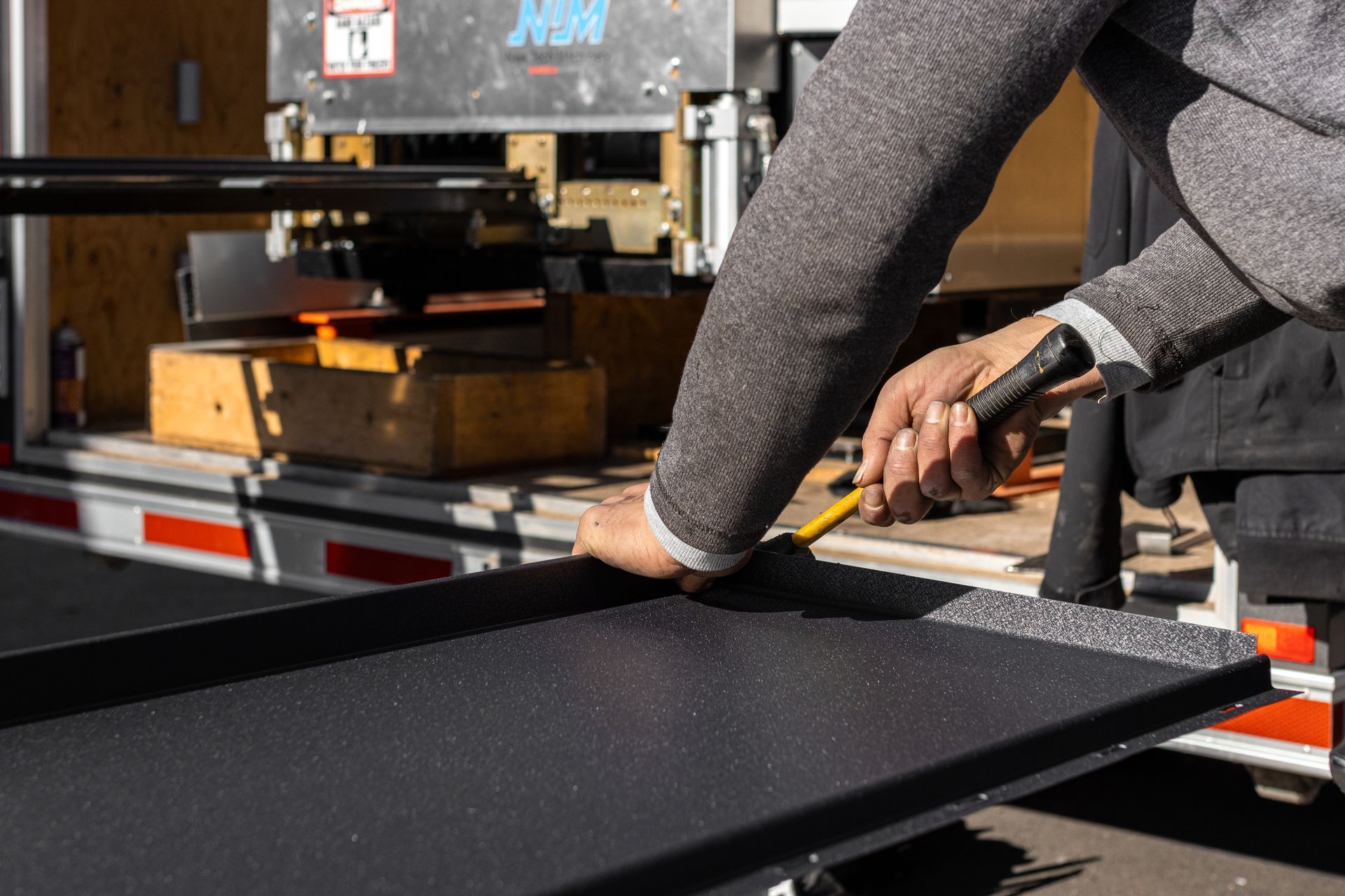 Person using a tool to work on a black metal surface, likely inside a trailer.