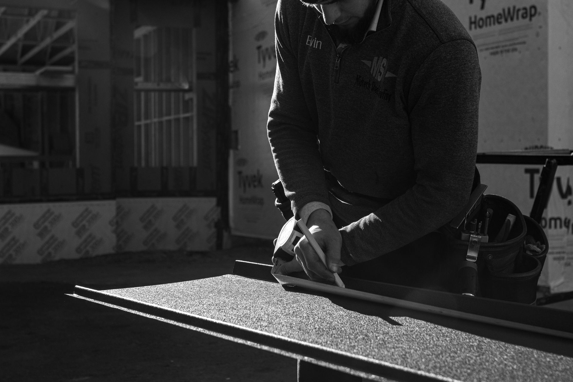 Construction worker cuts material with a utility knife outdoors. Sunlight casts shadows.