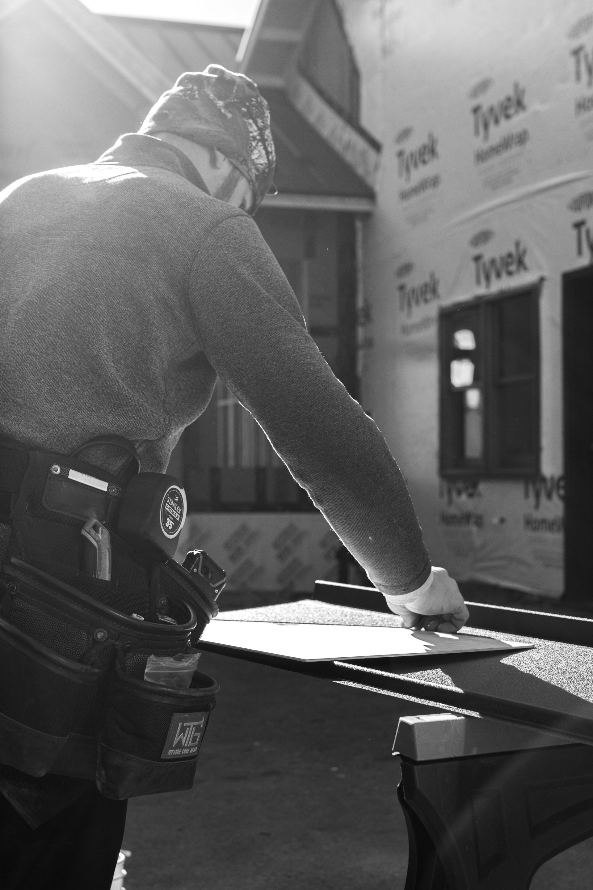 Construction worker in work clothes, working on a project, outside with a partially completed house in the background.