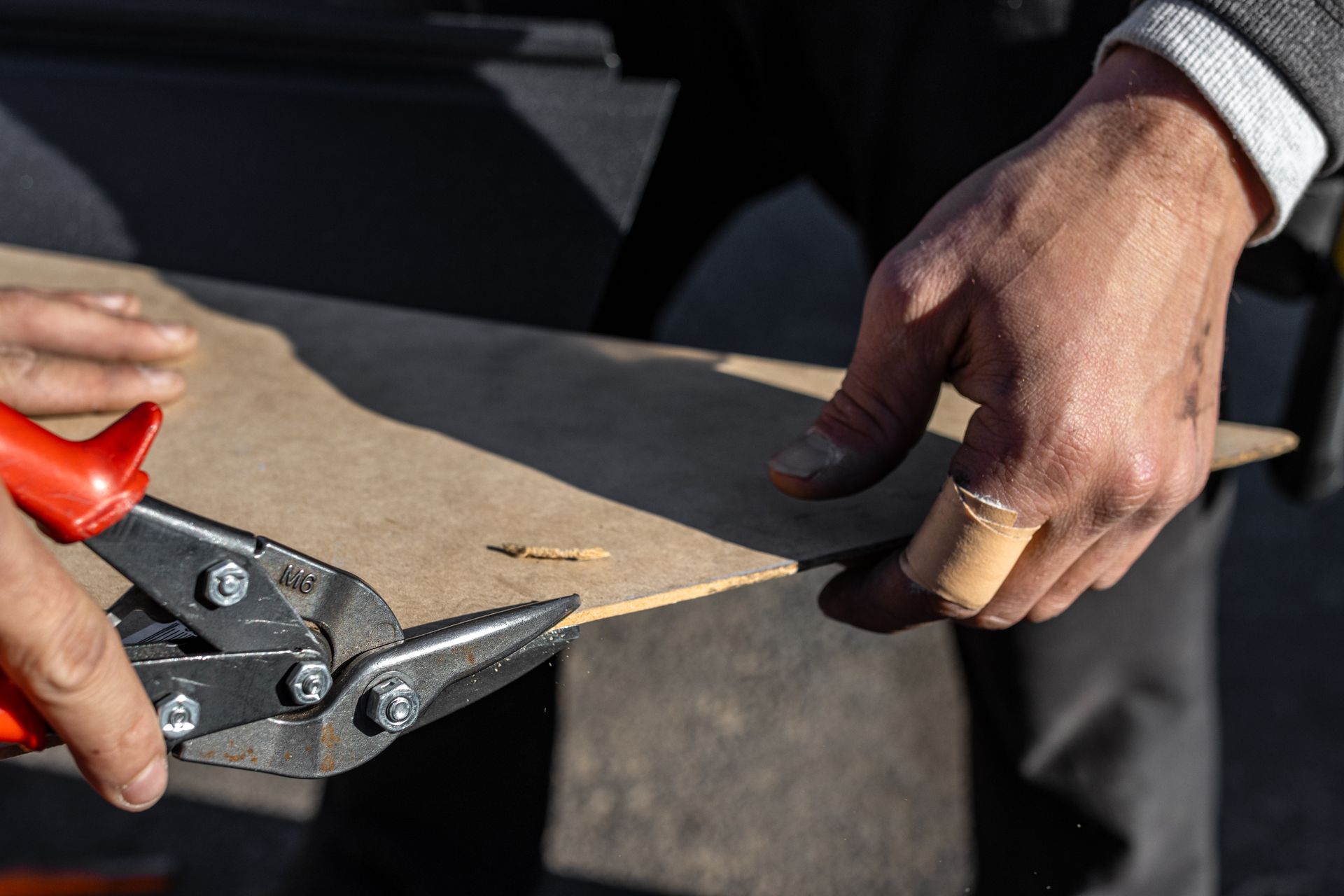 Person using metal shears to cut a piece of brown material, with a bandaged finger.