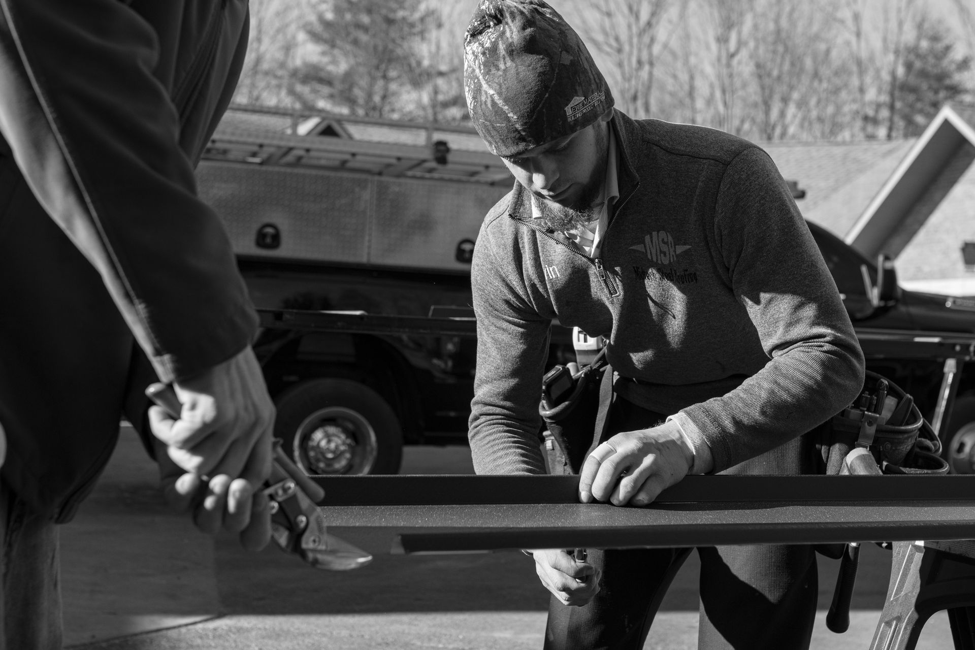 Two construction workers cutting metal outside, with truck in the background.