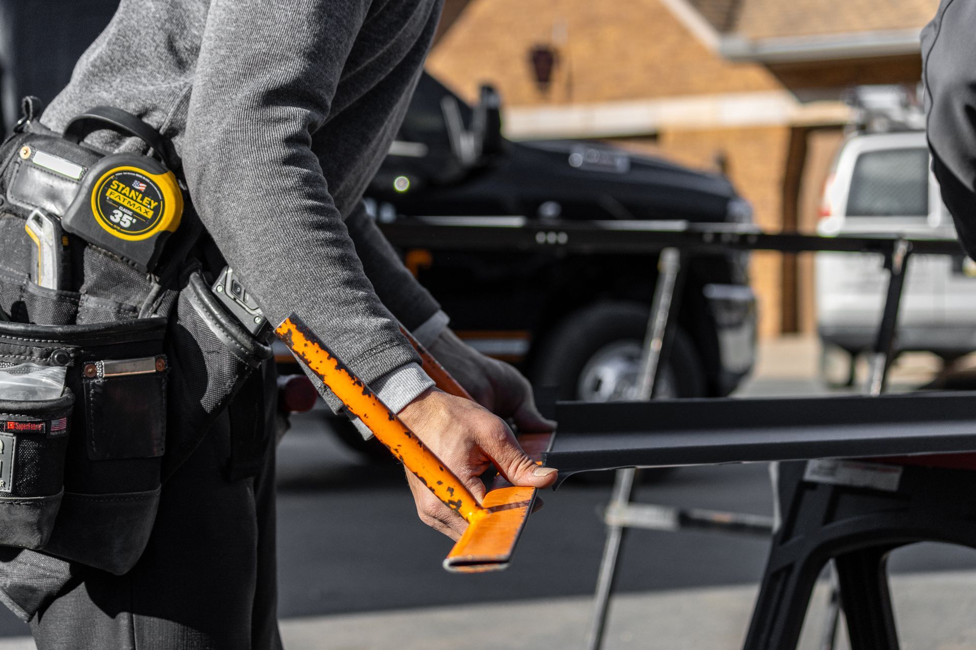 Person in gray work clothes using a hand tool to measure or cut a black metal piece.