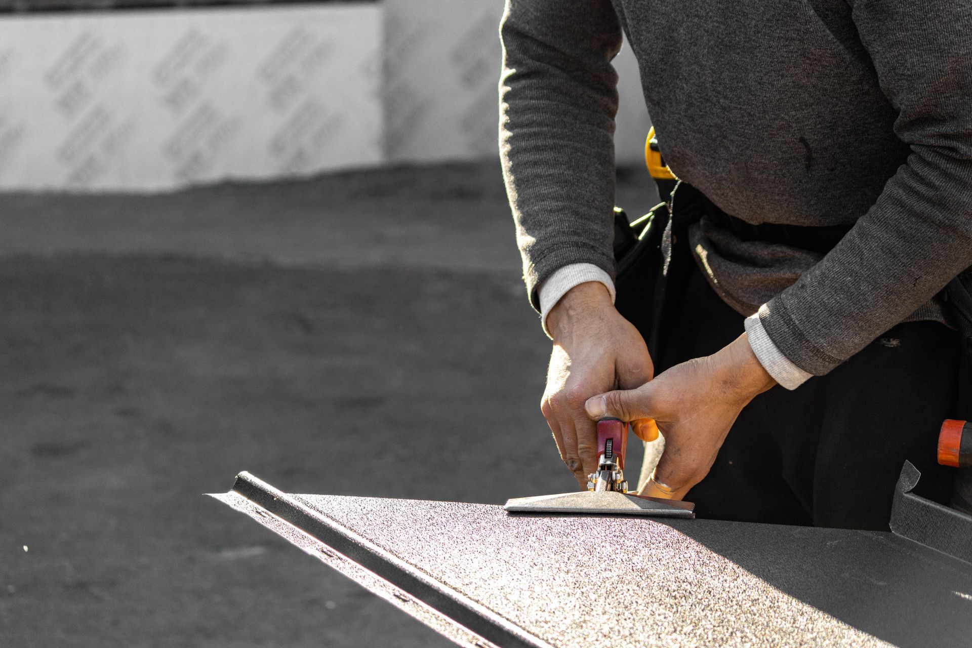 Person using a tool to work on a dark surface; outdoor setting.