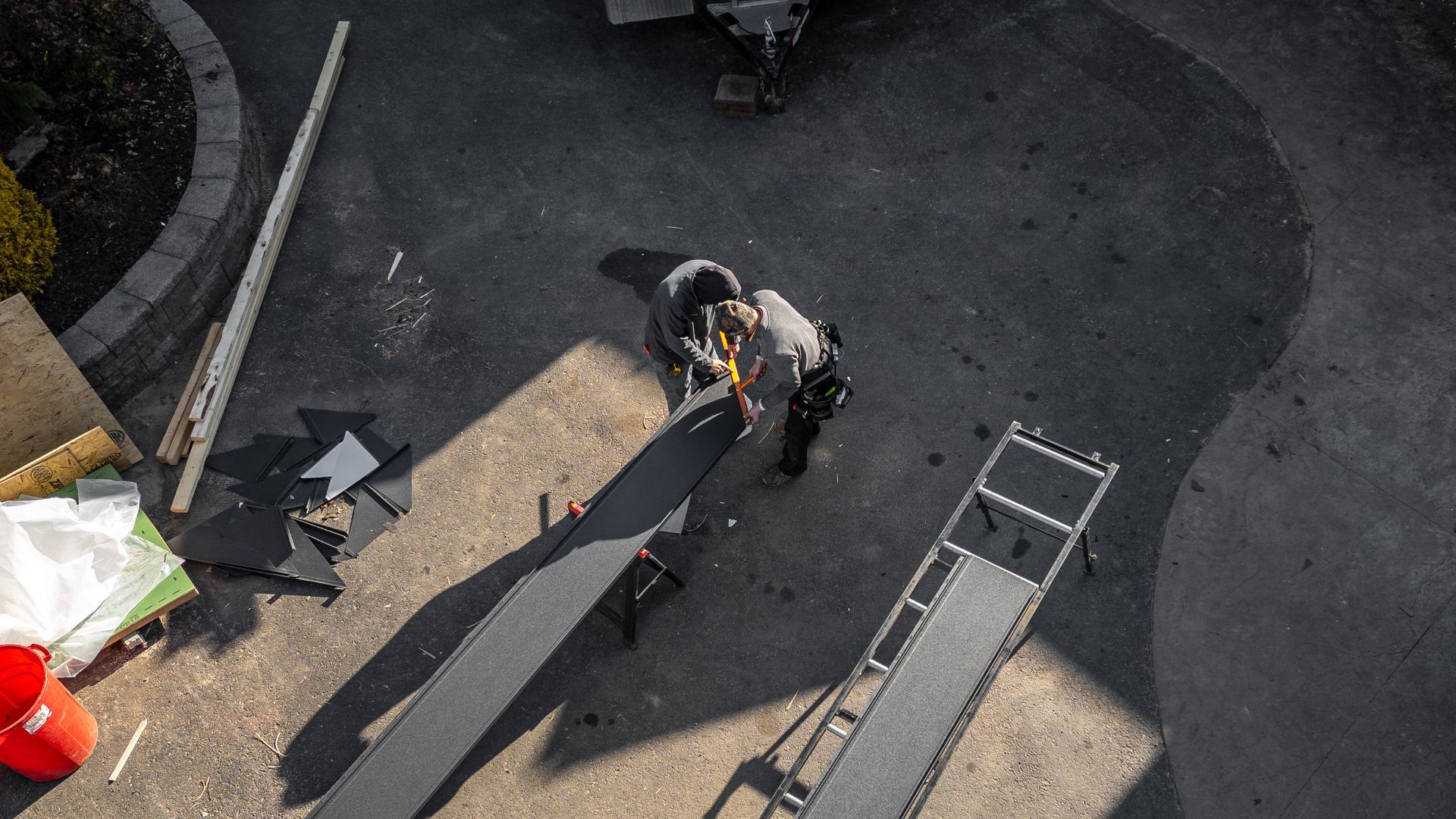 Overhead view of a person cutting wood on a ramp in a driveway, with tools and materials nearby.
