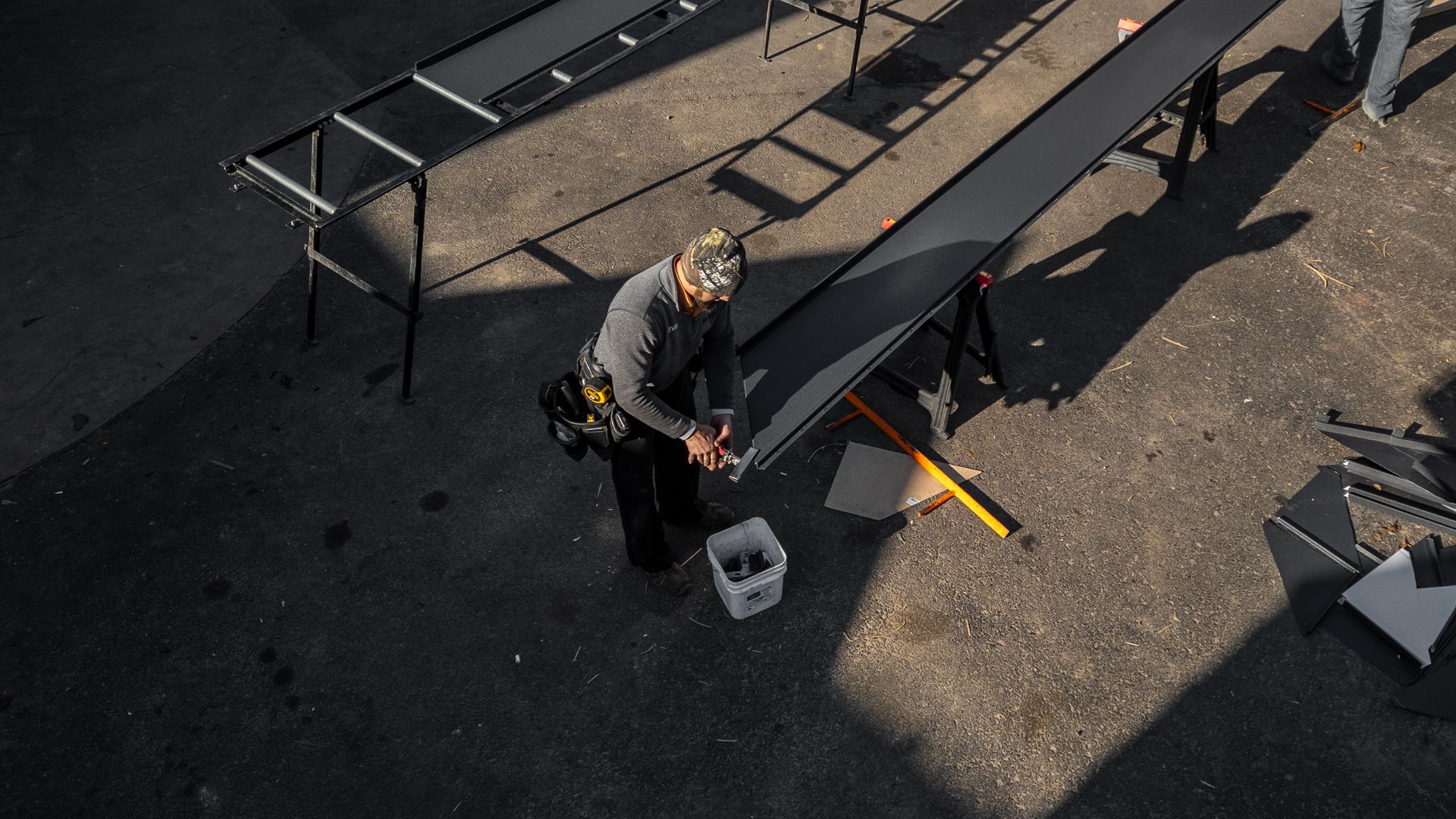 Person working on long, dark metal panels set on sawhorses outdoors.
