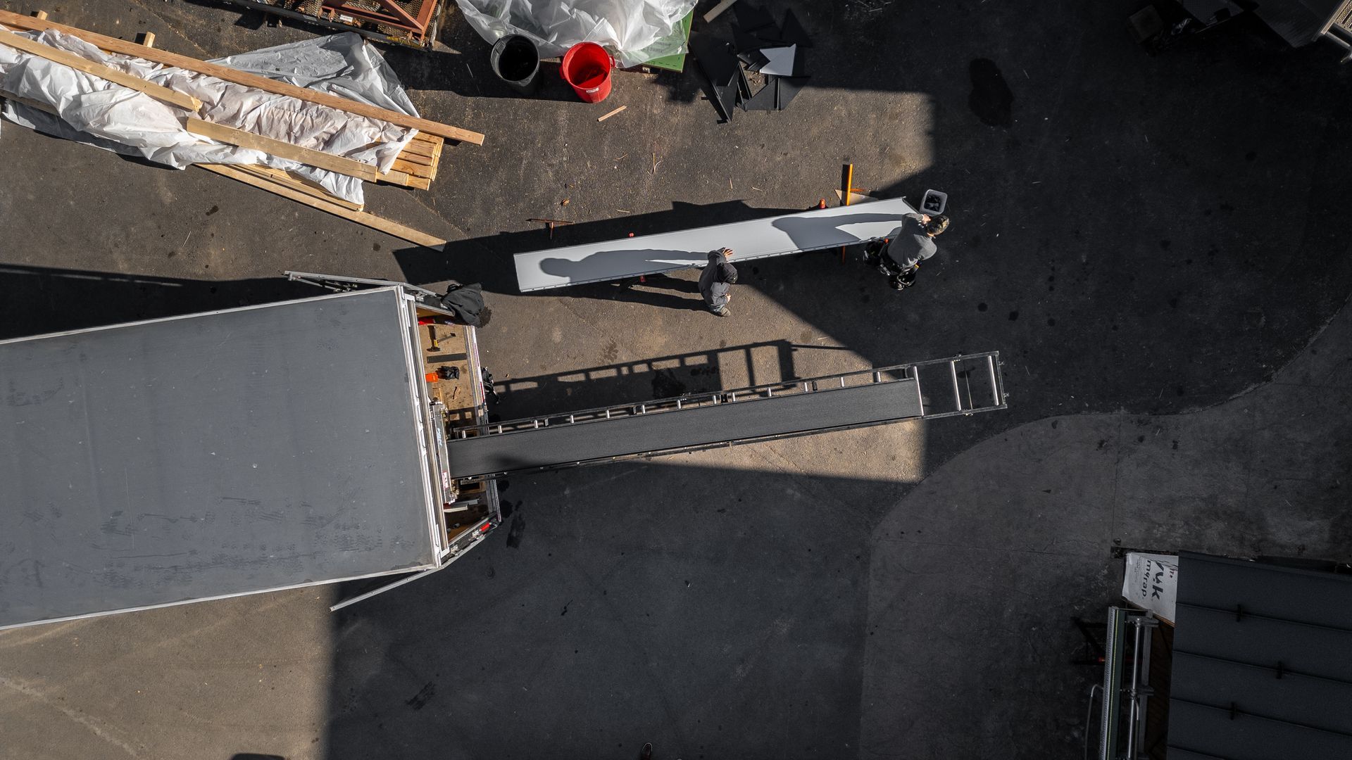 Overhead view of a loading dock with a gray truck, a ramp, and construction materials nearby.