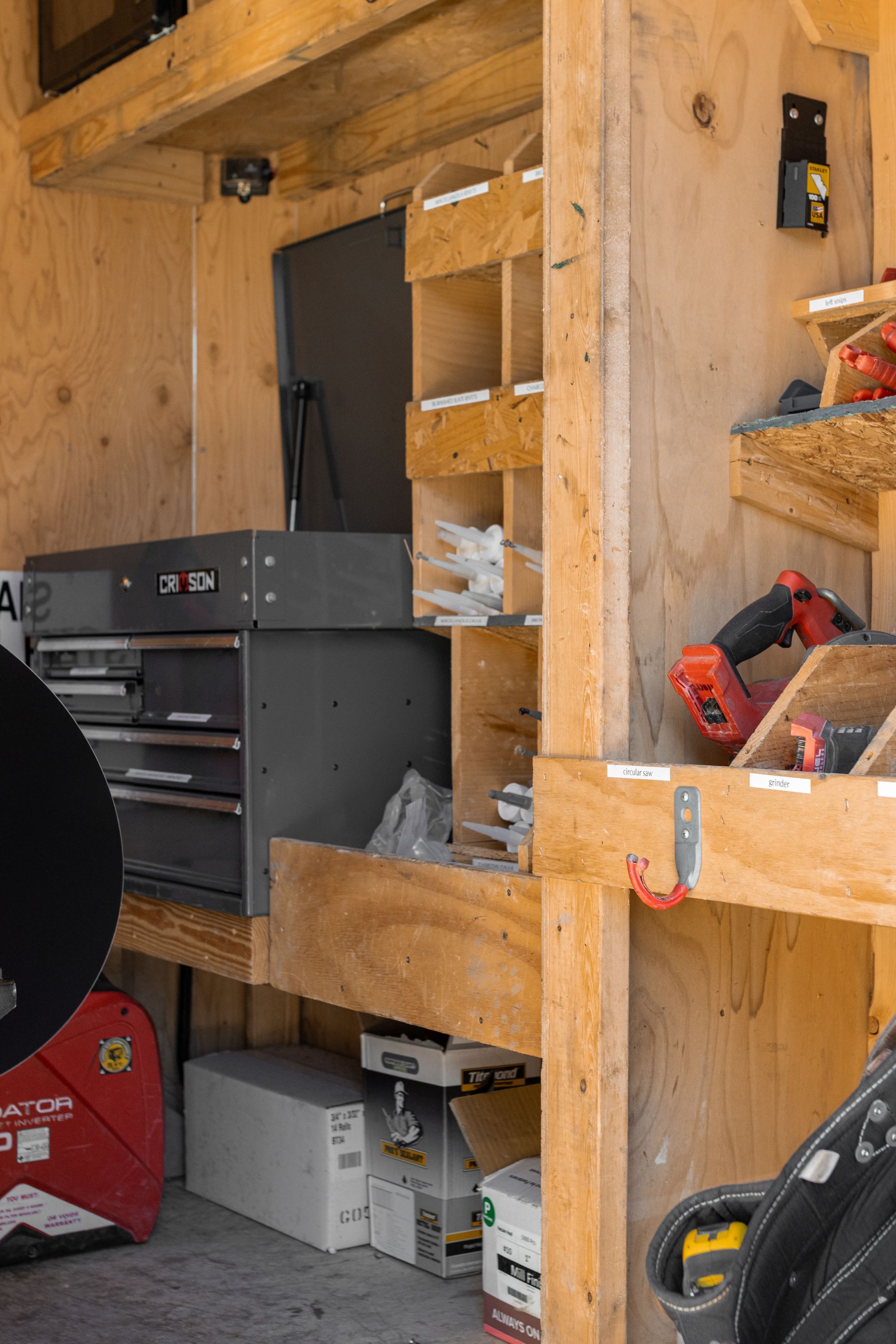 Interior of a work van with tools, storage, and a toolbox. Wooden shelves and paneling.