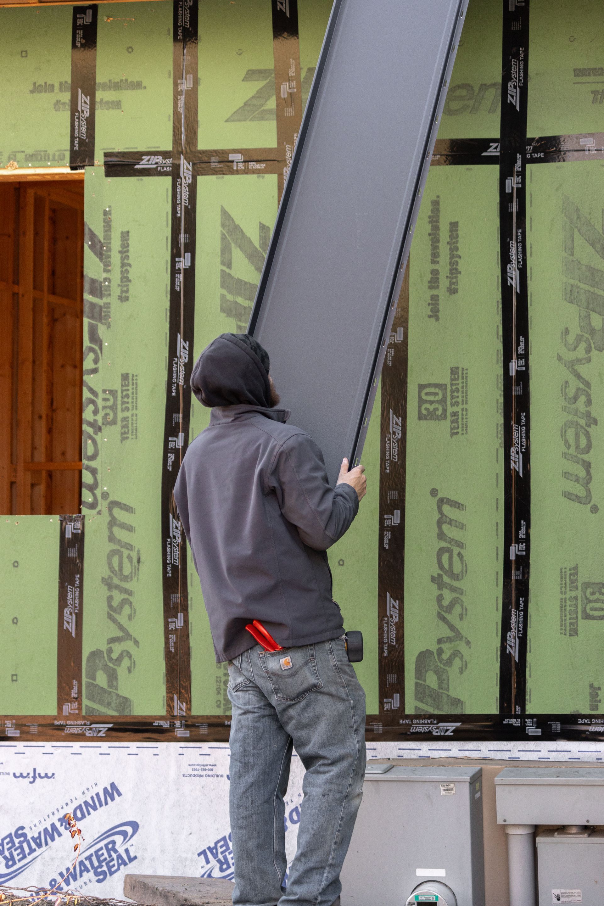 Construction worker carrying a large gray panel outside a building under construction.
