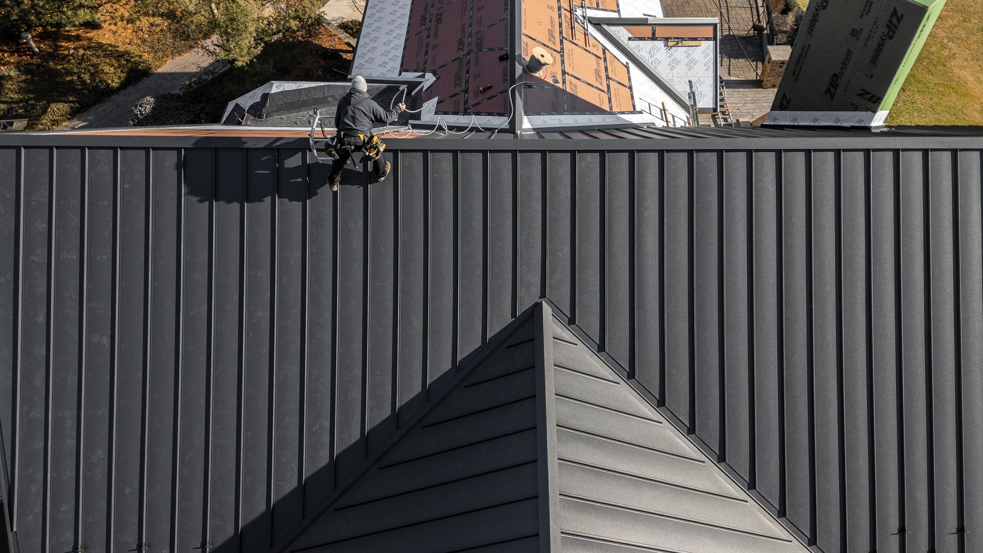Roofer in gray outfit working on a black metal roof, with a triangular roof section in the foreground.