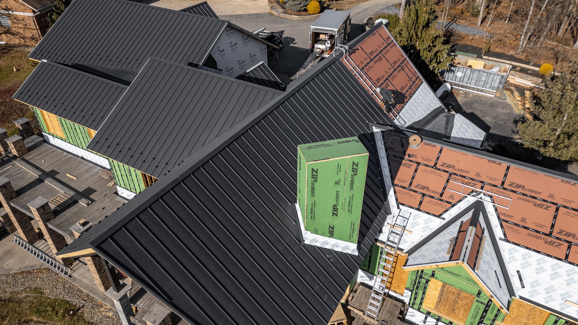 Aerial view of a house with black metal roofing under construction, a green chimney, and exposed framework.