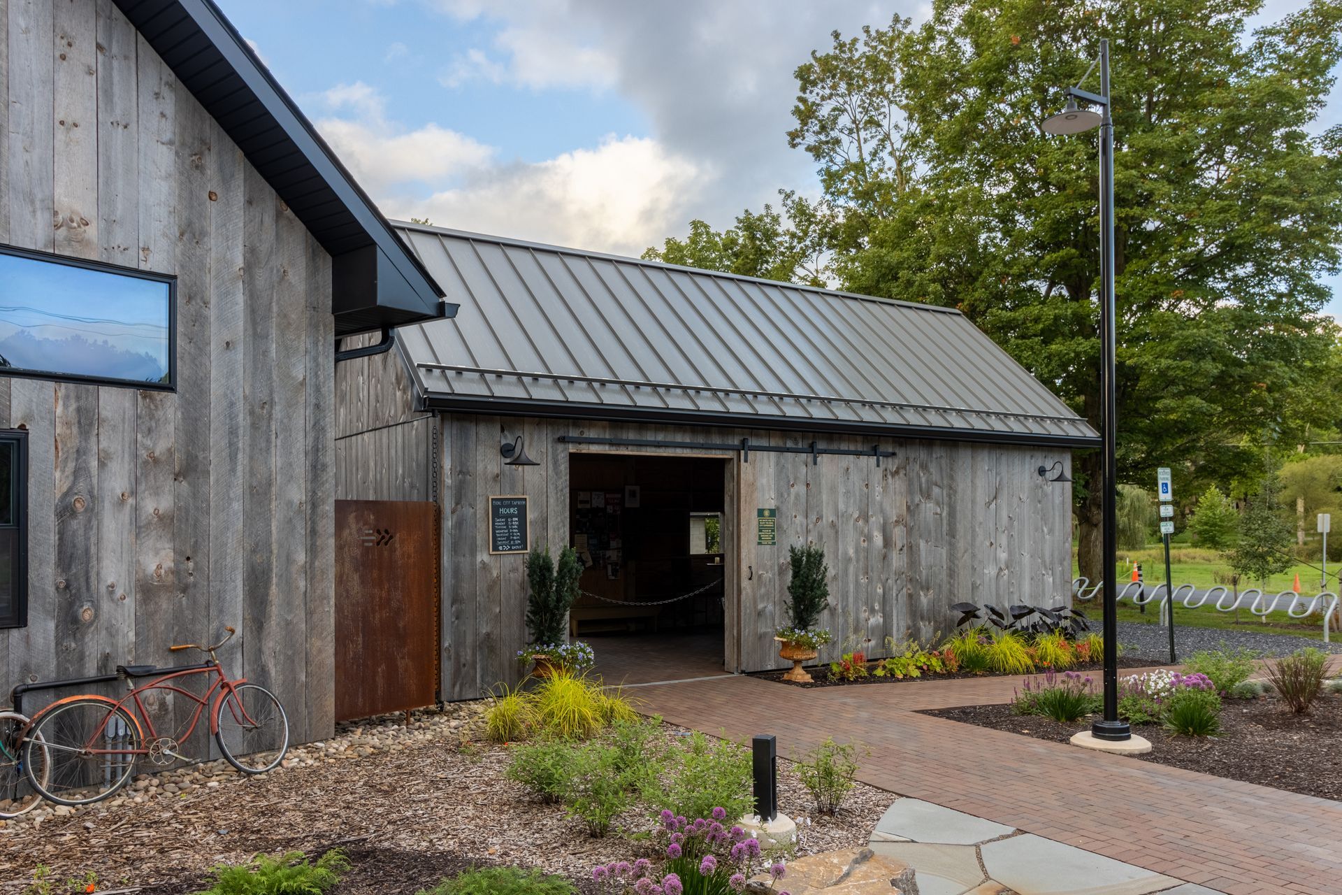 Weathered wooden barn entrance with open doorway, metal roof, and stone path.