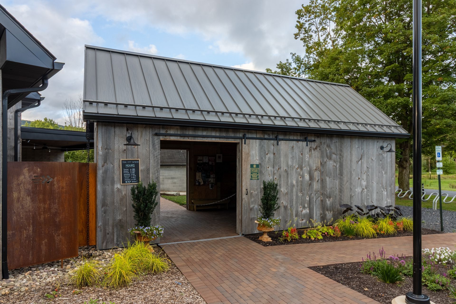 Weathered wooden shed with metal roof, brick pathway, and greenery.