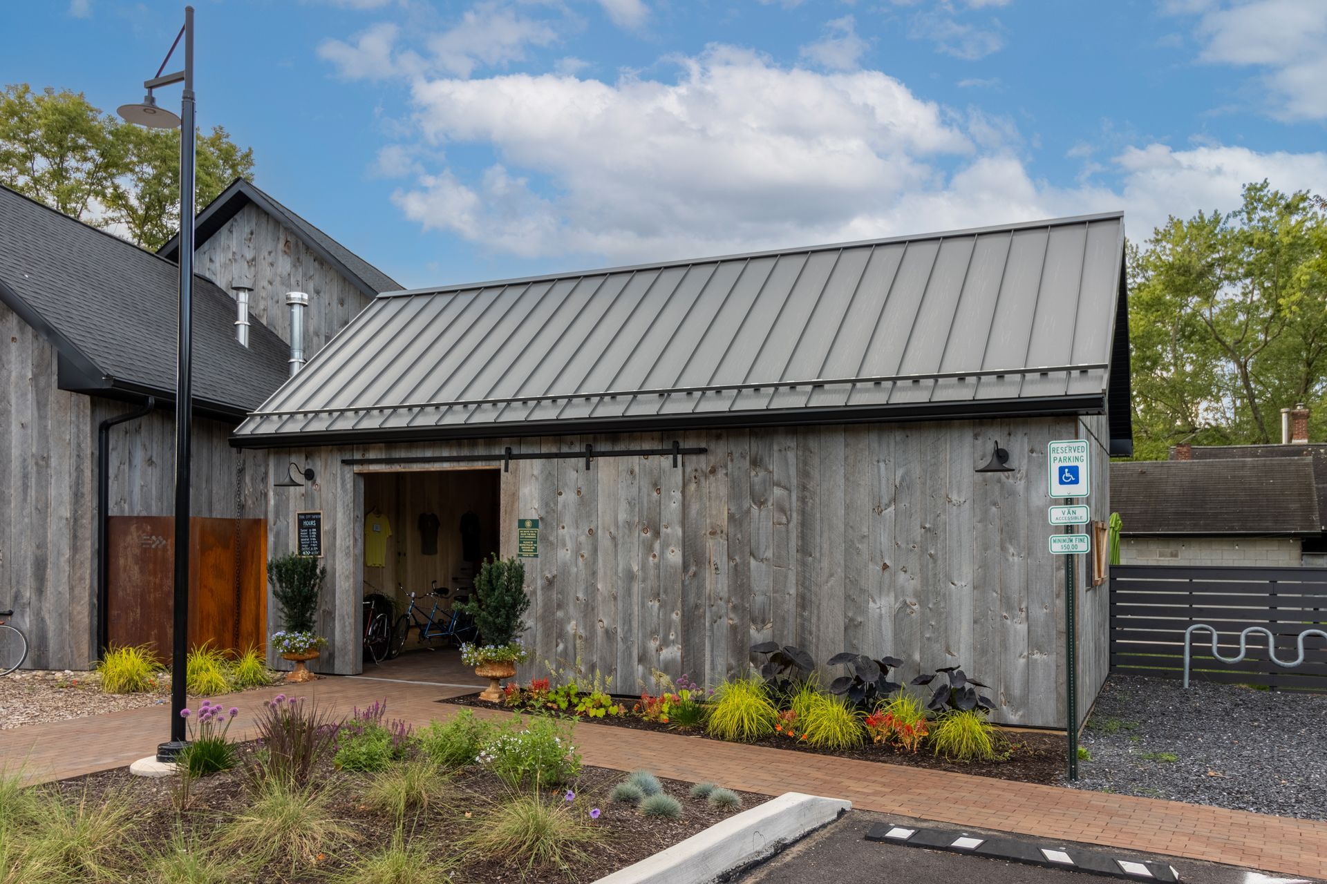Exterior view of a weathered gray barn-like building with a metal roof and accessible parking sign.