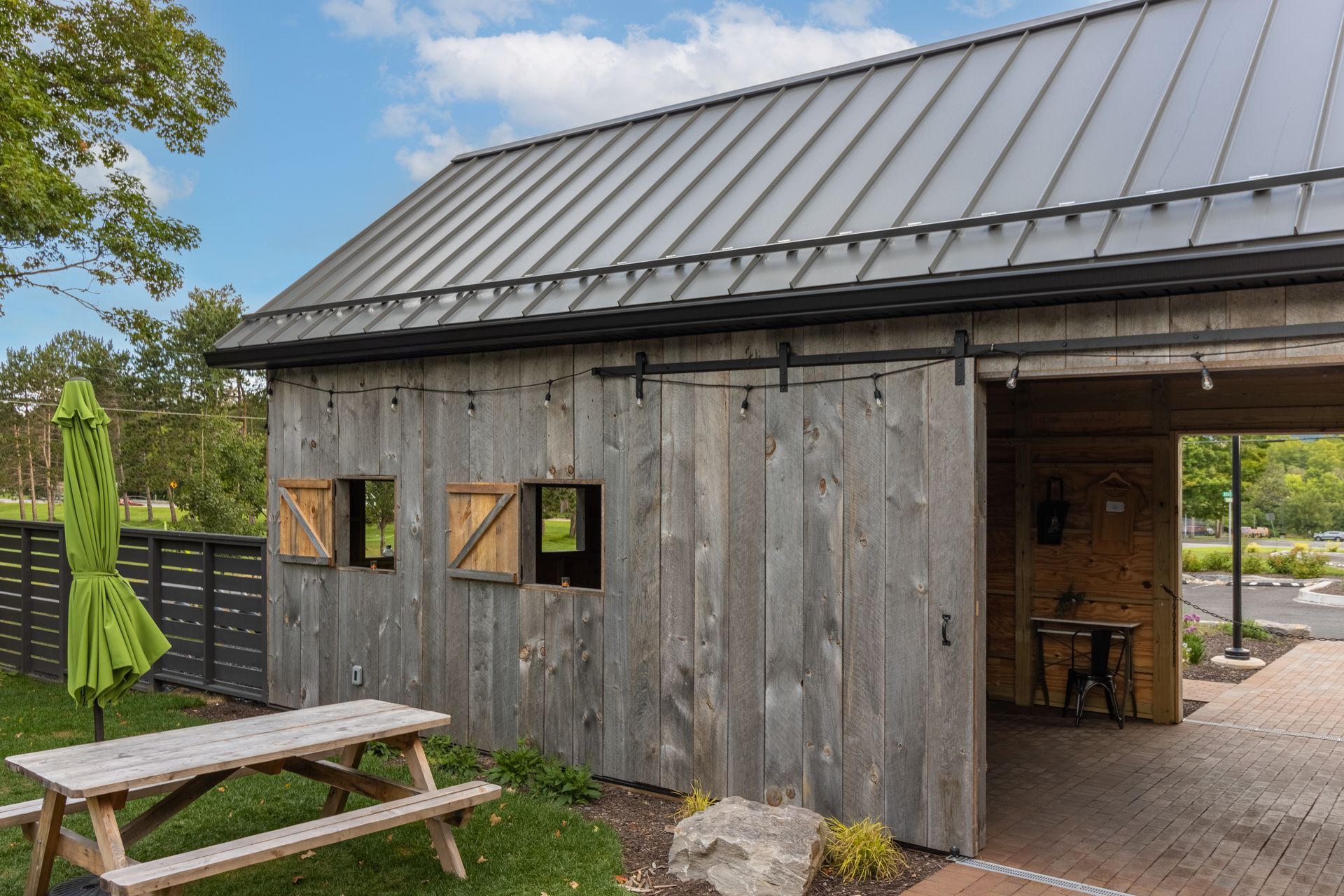Weathered barn-style building with sliding doors, picnic table, and green umbrella on the lawn.