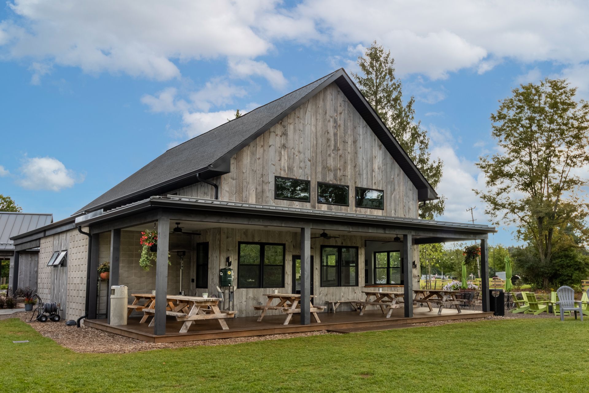 Rustic, gray-sided building with a porch, picnic tables, and a green lawn under a blue sky.