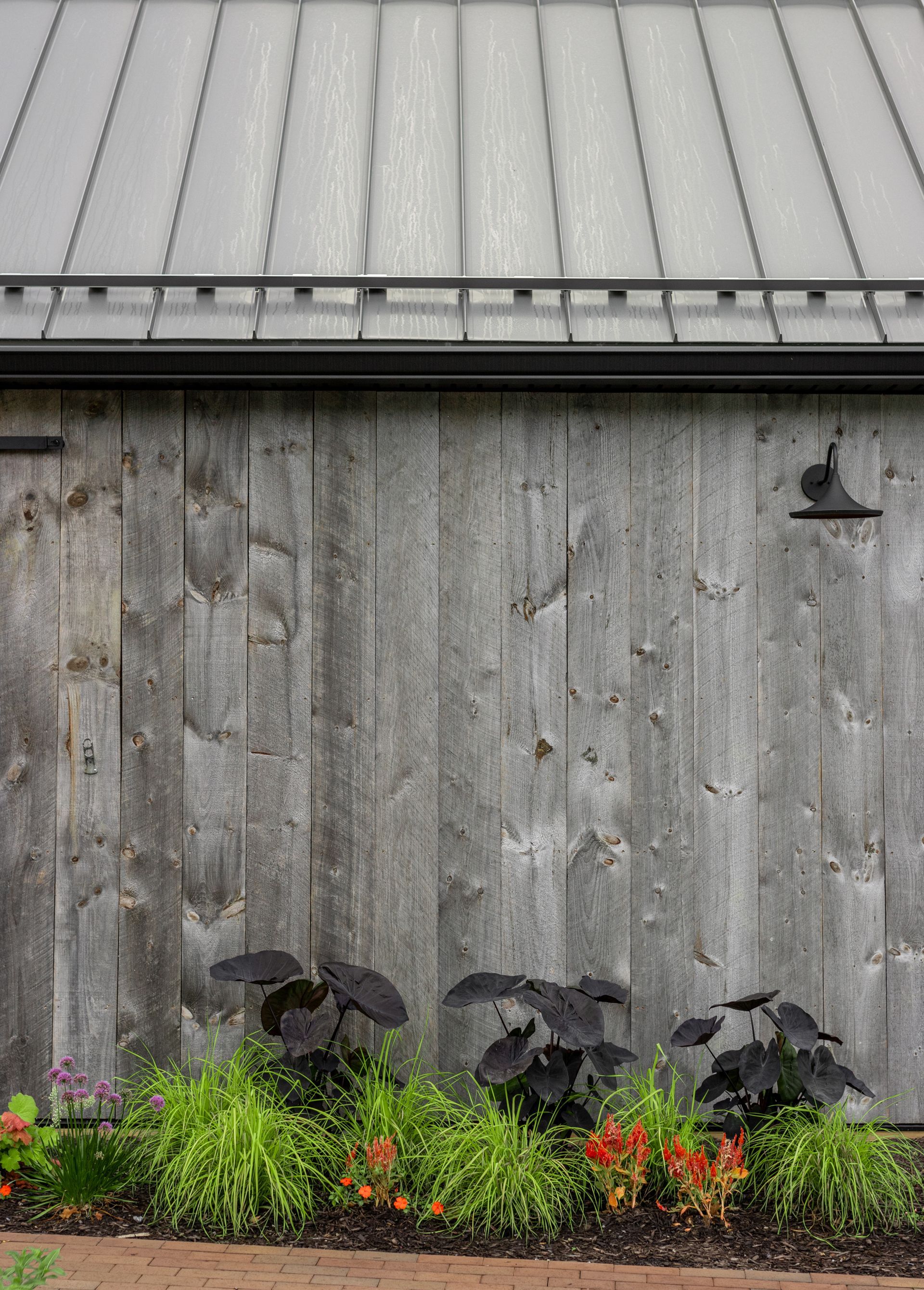 Weathered wooden barn wall with metal roof and a garden bed.