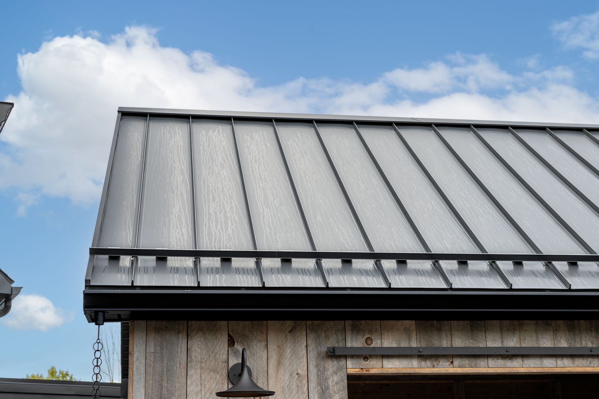 Gray metal roof on a wooden building with black trim against a blue sky with clouds.