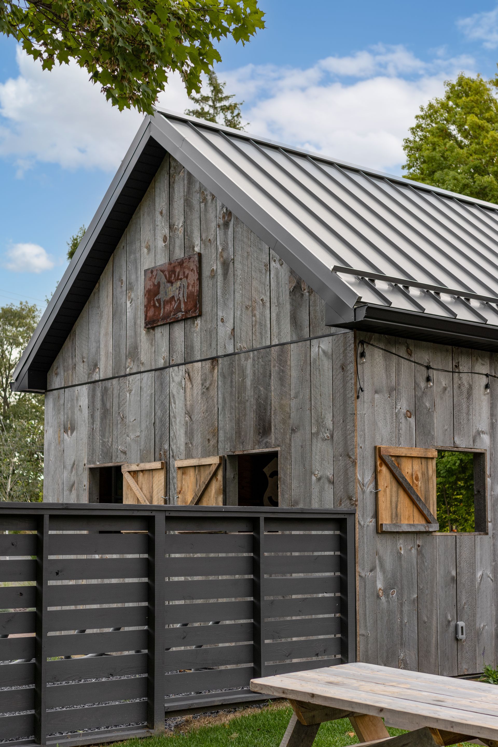 Weathered gray barn with metal roof and black fence, picnic table, and wooden shutters.