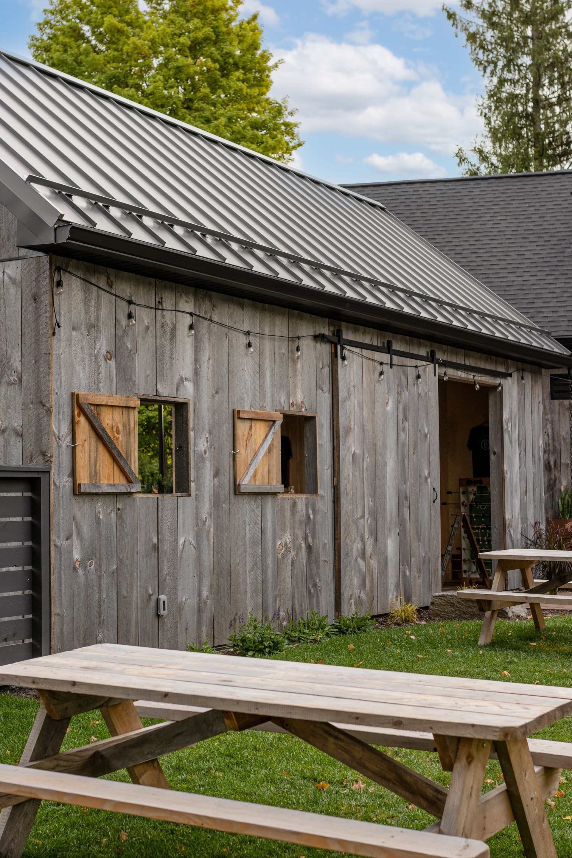 Weathered gray barn with picnic tables on green grass.