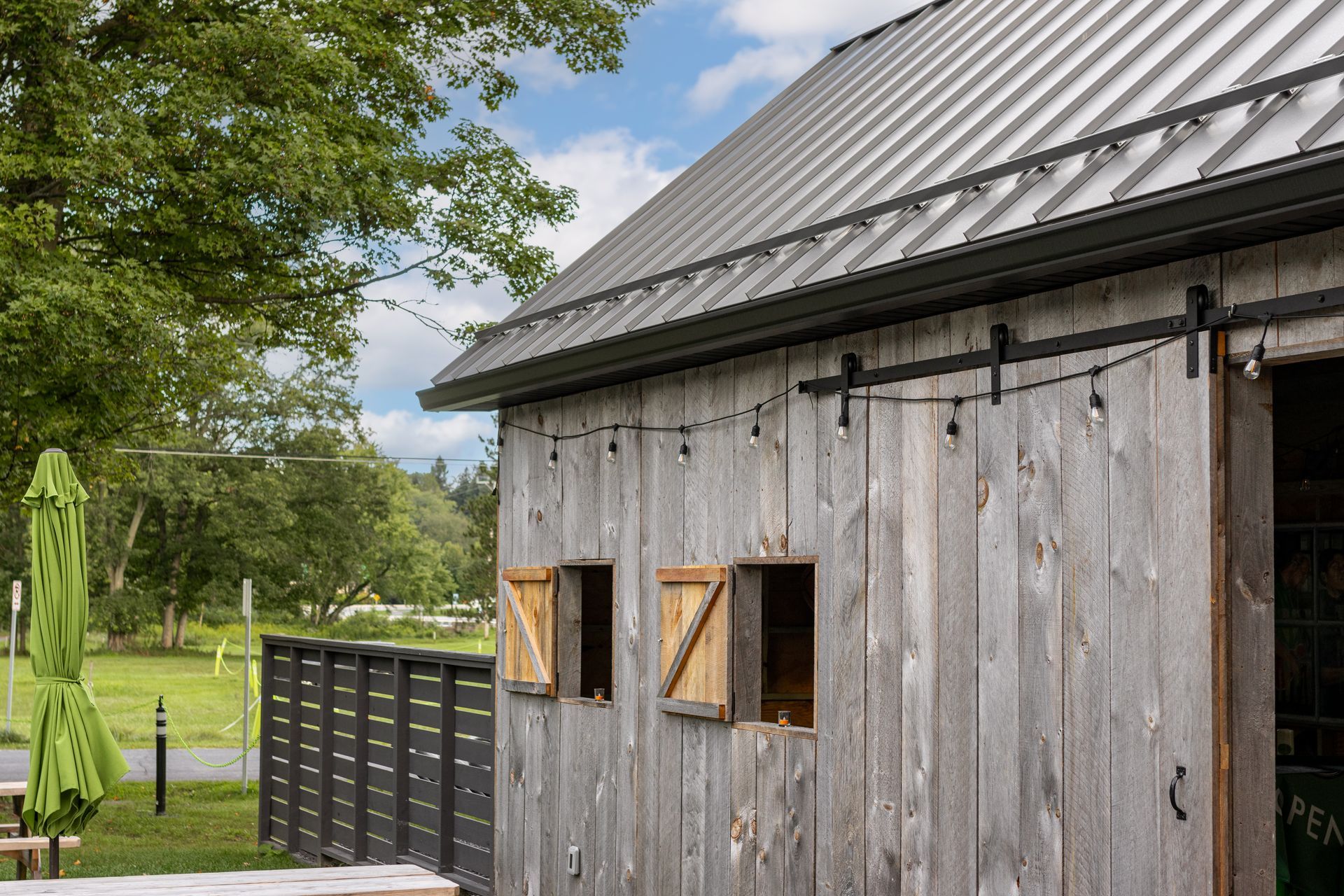 Weathered wood barn with metal roof, string lights, and open window shutters.