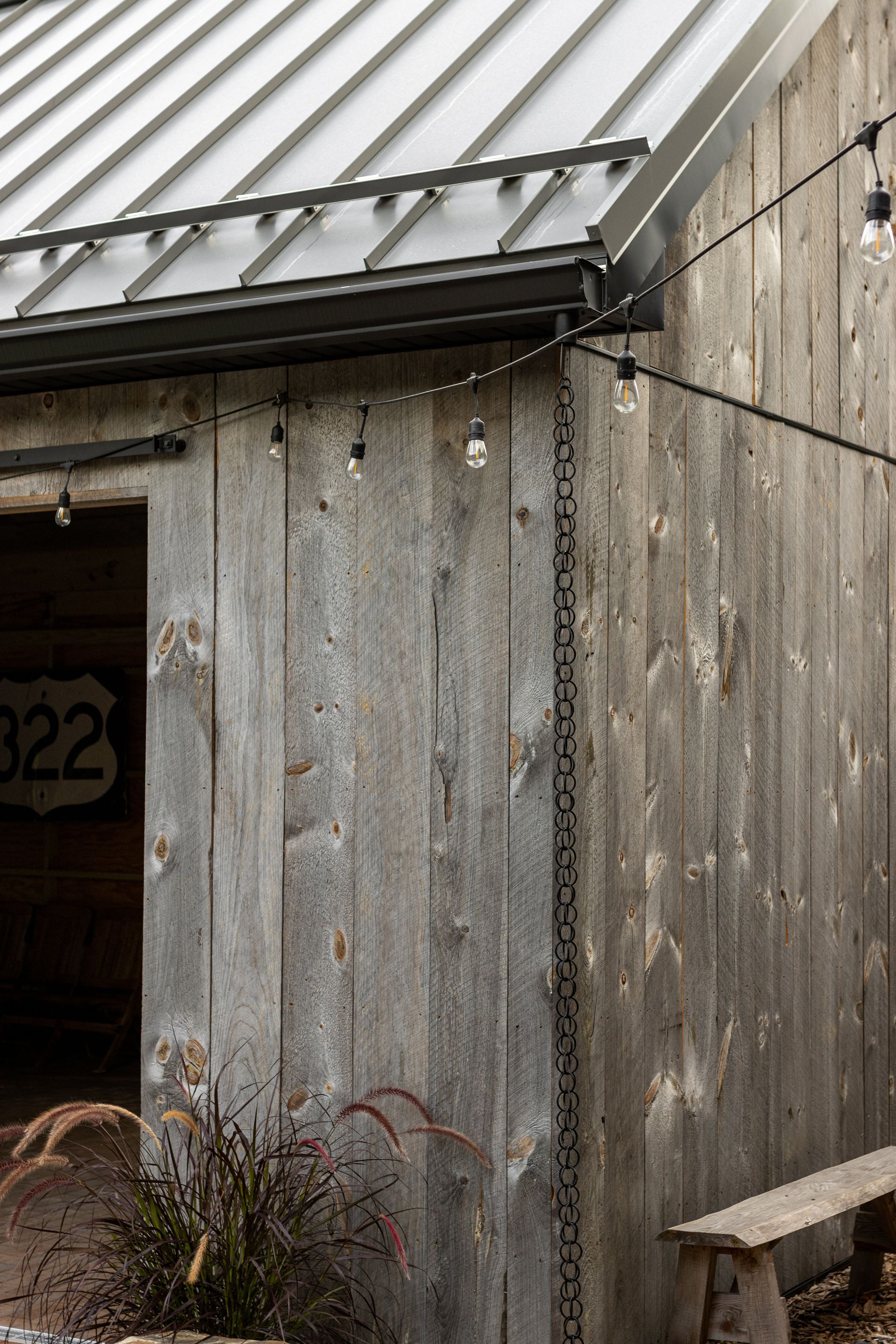 Weathered wood shed with a metal roof, string lights, and a rain chain.