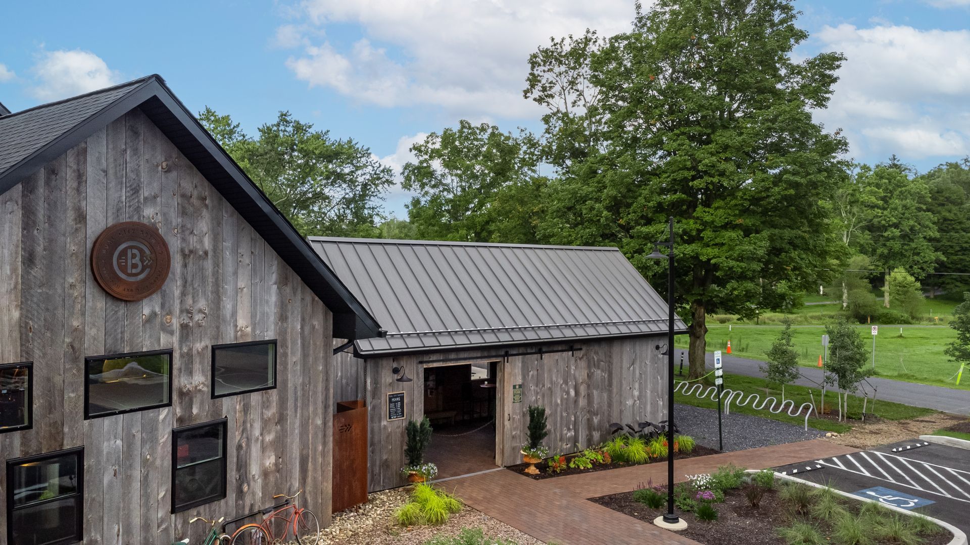 Rustic gray barn with black roof, open doorway, and surrounding greenery.