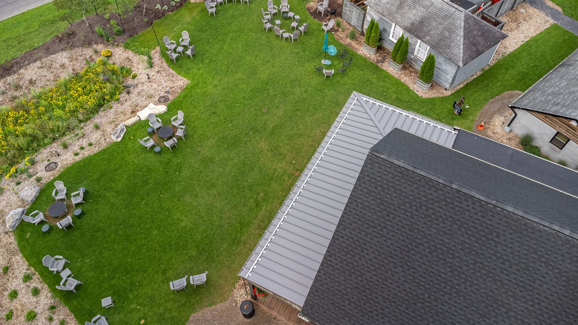 Overhead view of green lawn with outdoor seating around tables, next to buildings with gray roofs.