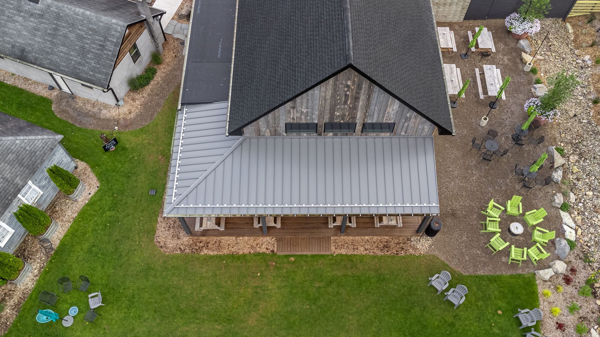 Overhead view of building with gray roof and porch, lawn with green chairs, and a fire pit area.