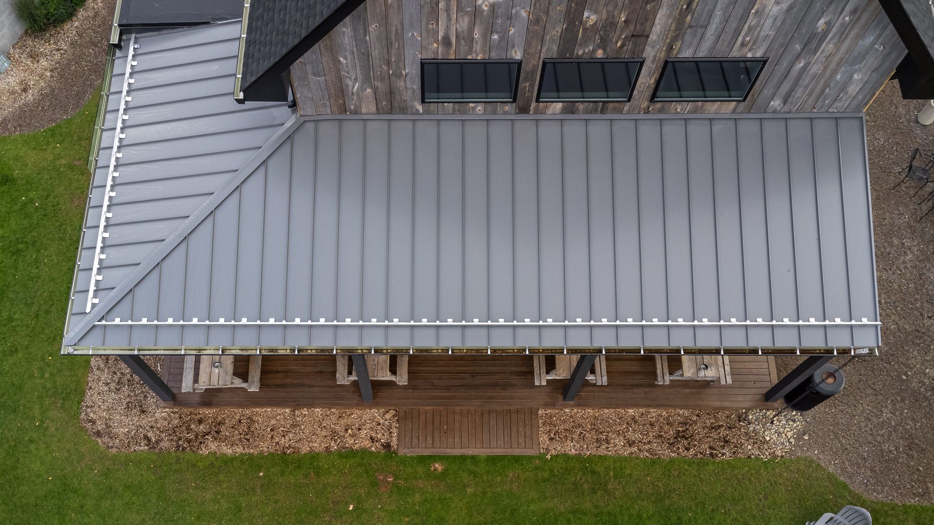 Overhead view of a porch with a gray metal roof and wooden beams, with chairs below.