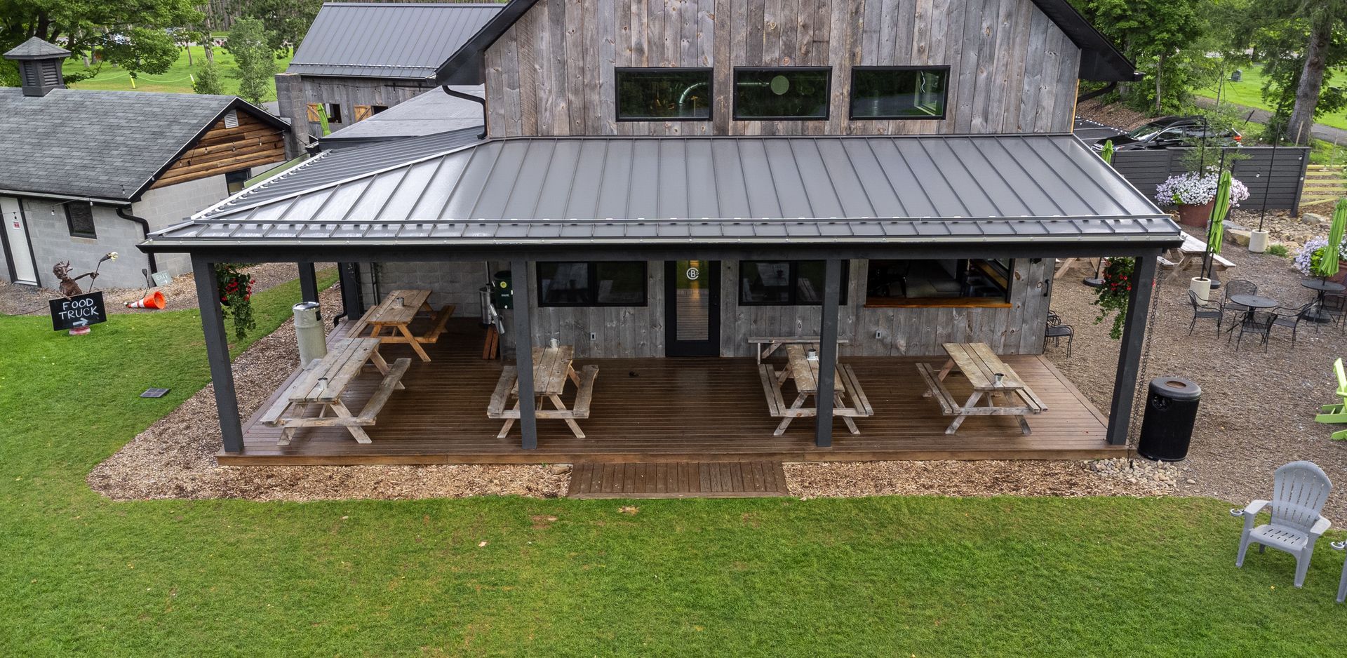 Rustic wooden building with a covered porch, picnic tables, and outdoor seating on a green lawn.