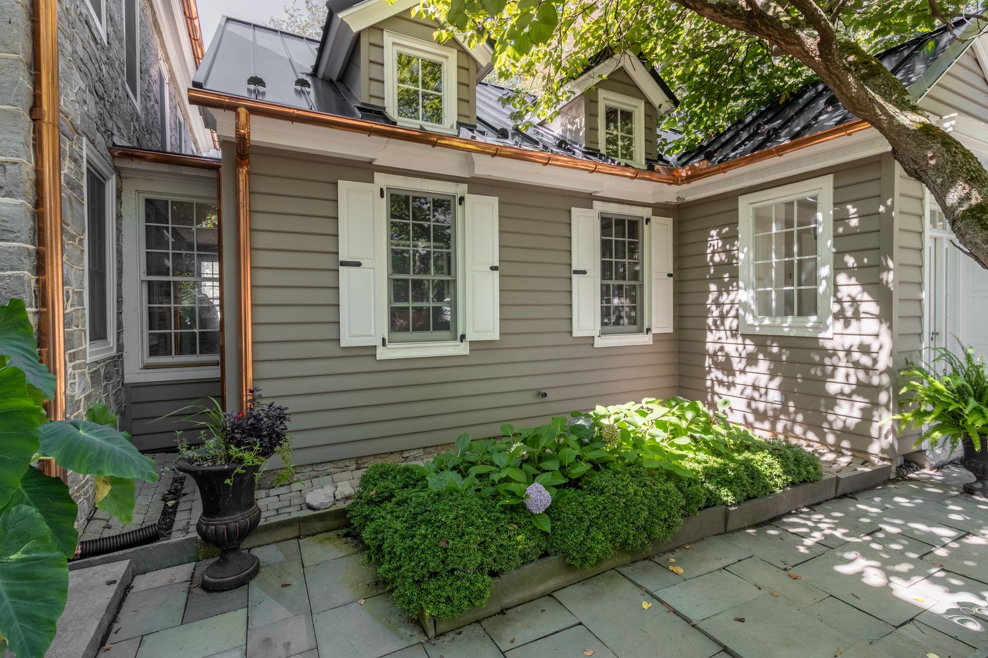 Exterior of a gray building with white shutters, copper gutters, and a garden.