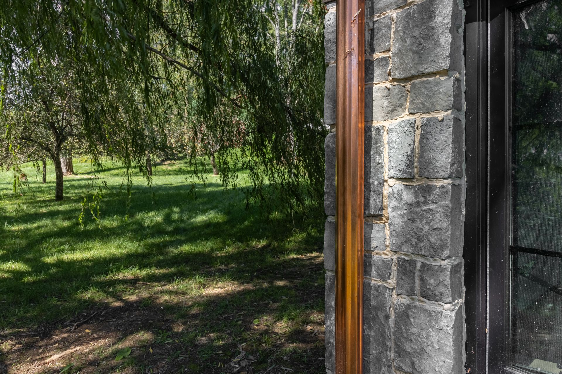 Exterior view of brick wall with brown wood trim, window, and a green lawn under trees.