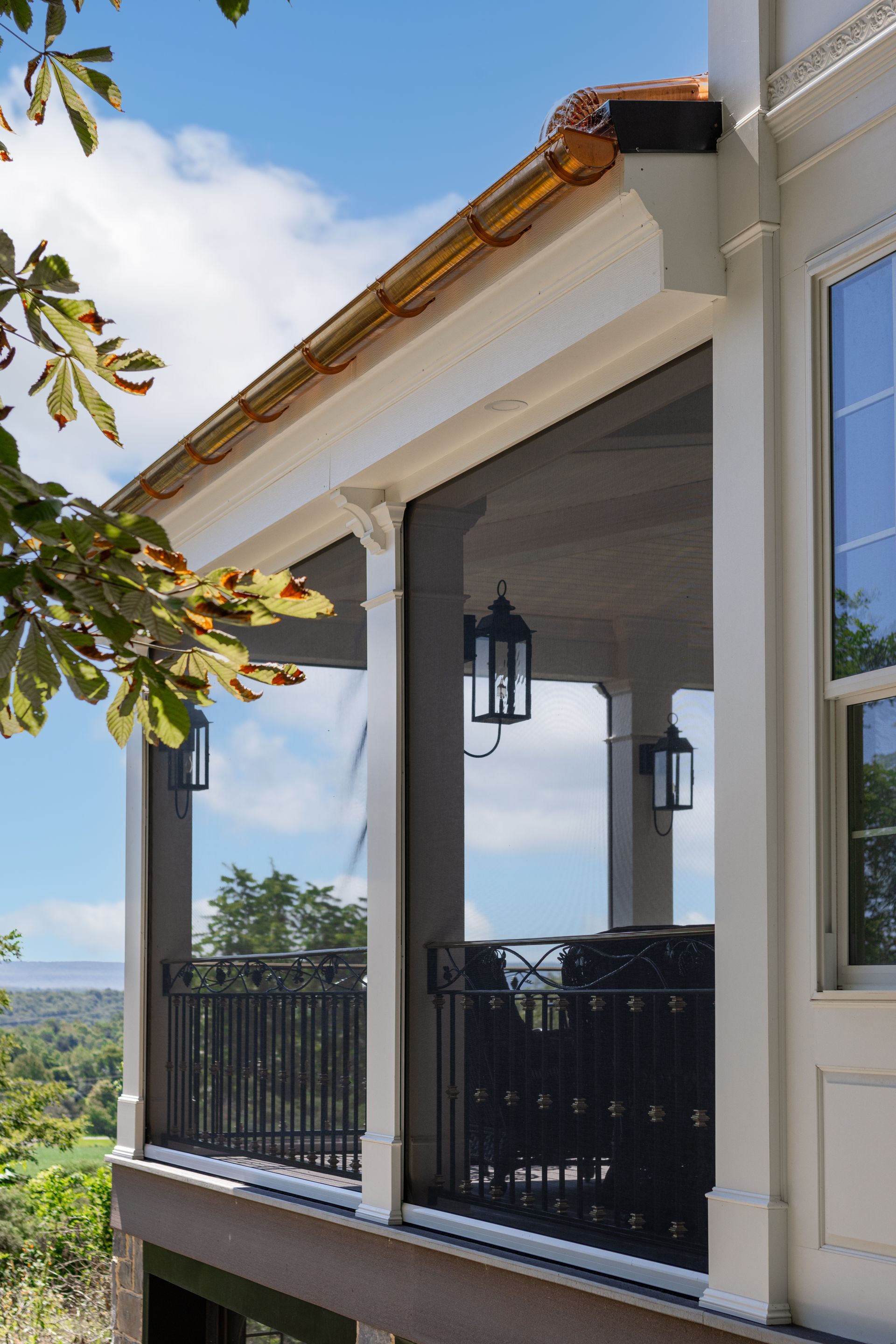 Screened porch with black railing, white trim, and hanging lanterns, overlooking a scenic landscape.