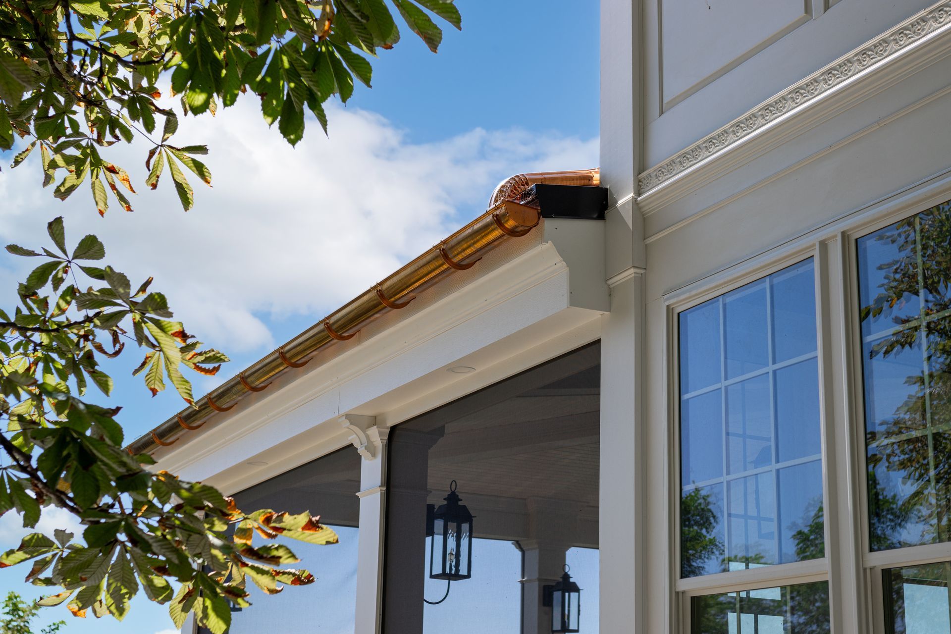 Copper gutters on a white house with blue sky and tree branches in the foreground.