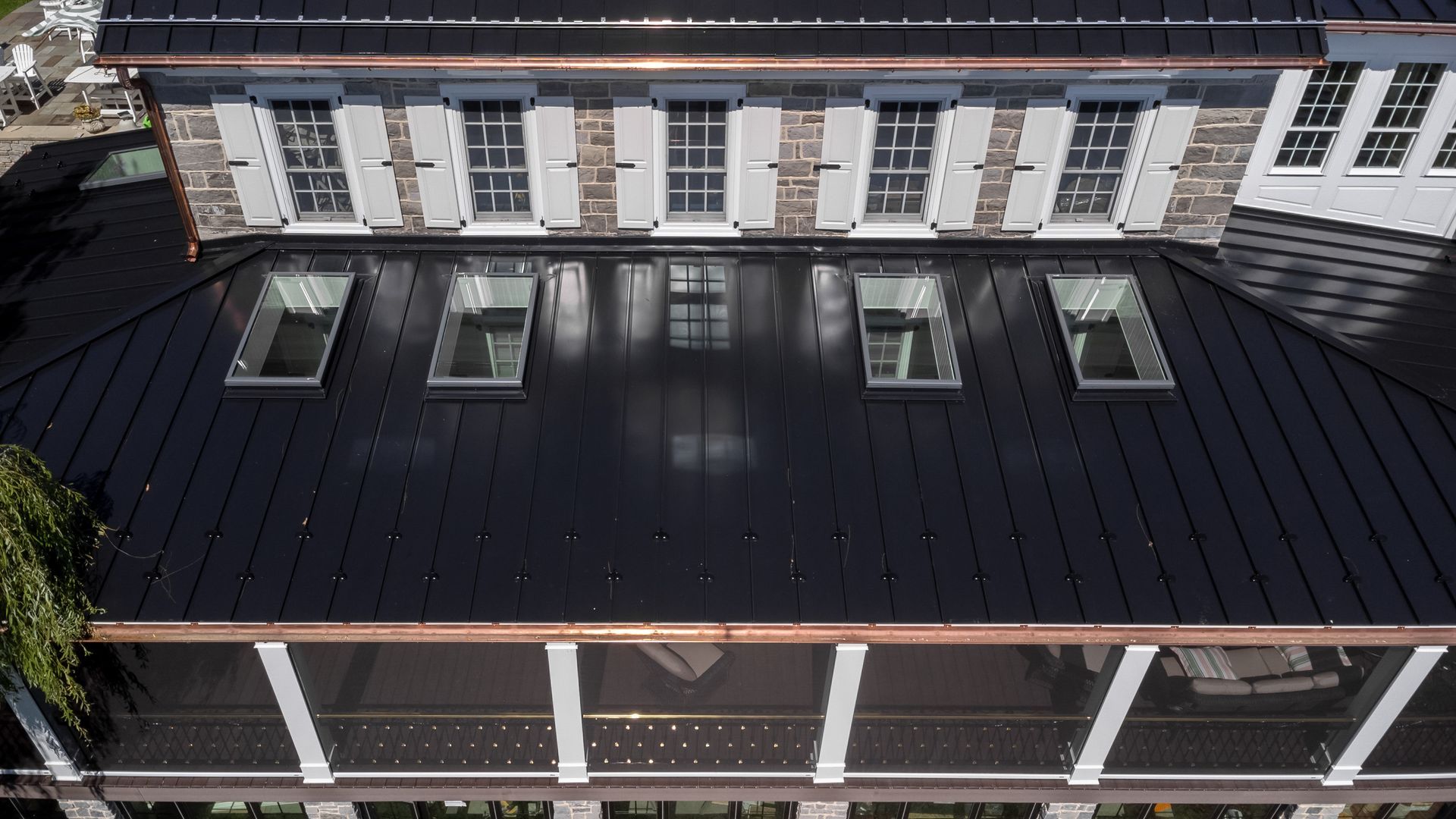 Black metal roof of a building with skylights, copper gutters, and stone facade with shutters.