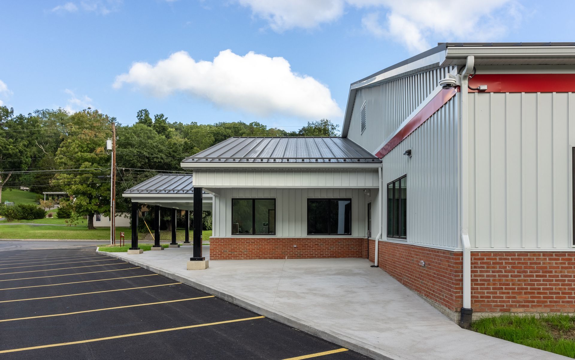 Building exterior with a parking lot; white siding, red trim, and a covered walkway.