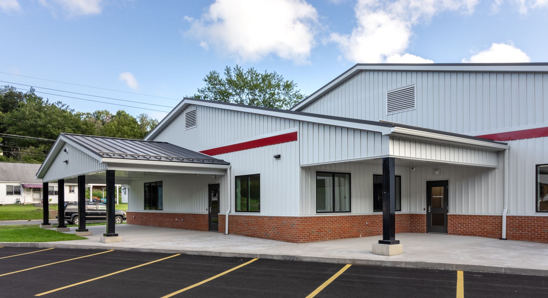 White building with black columns, red trim, and a brick base, with a parking lot.