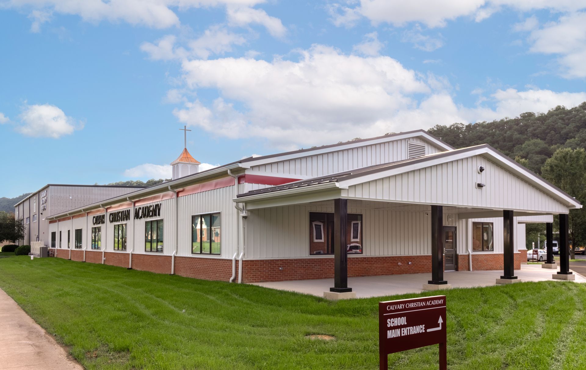 Church building with white siding, brick base, and green lawn. A cross on the steeple.