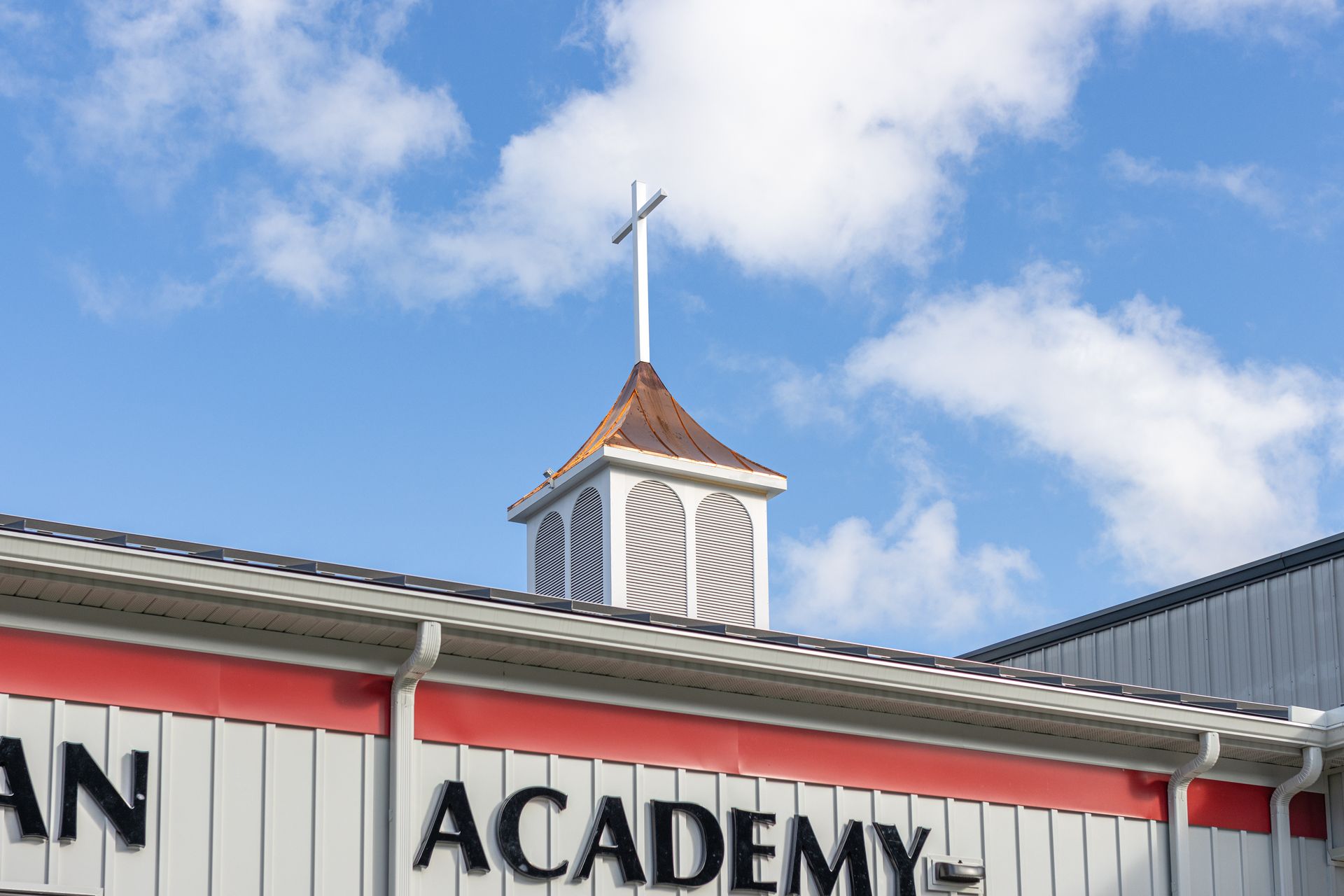 School building with cupola and cross, blue sky background.