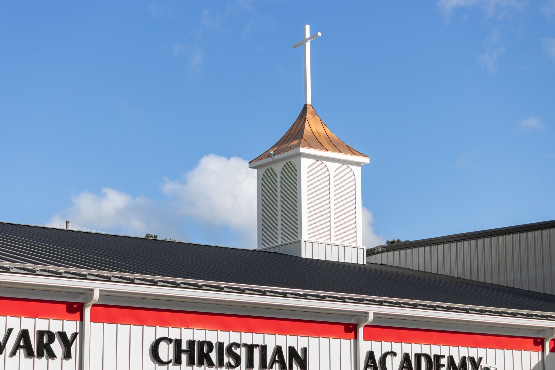 Calvary Christian Academy building with a white steeple and cross, against a blue sky.