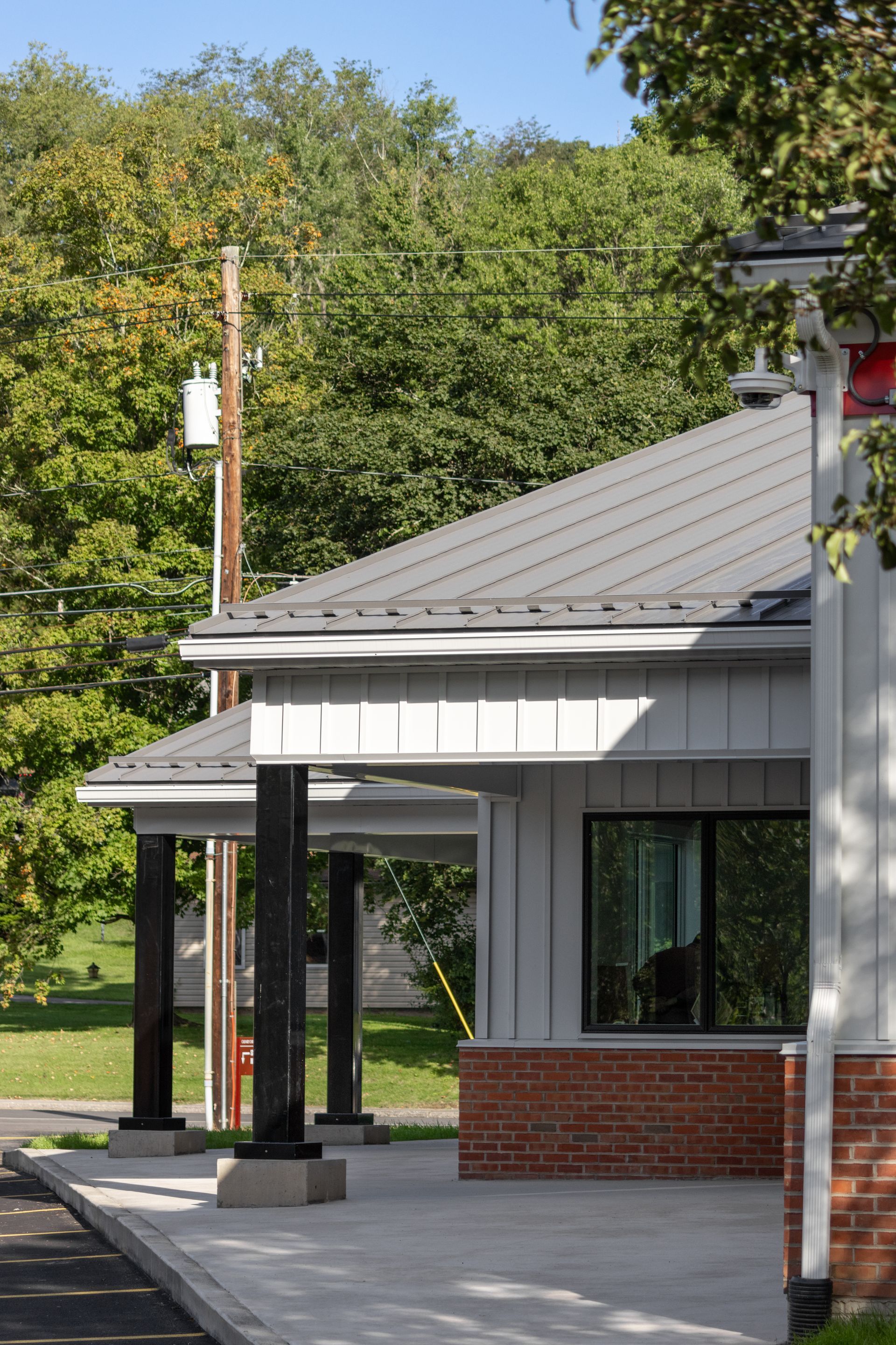 Modern gray building with black pillars and a brick facade, set against a backdrop of trees.