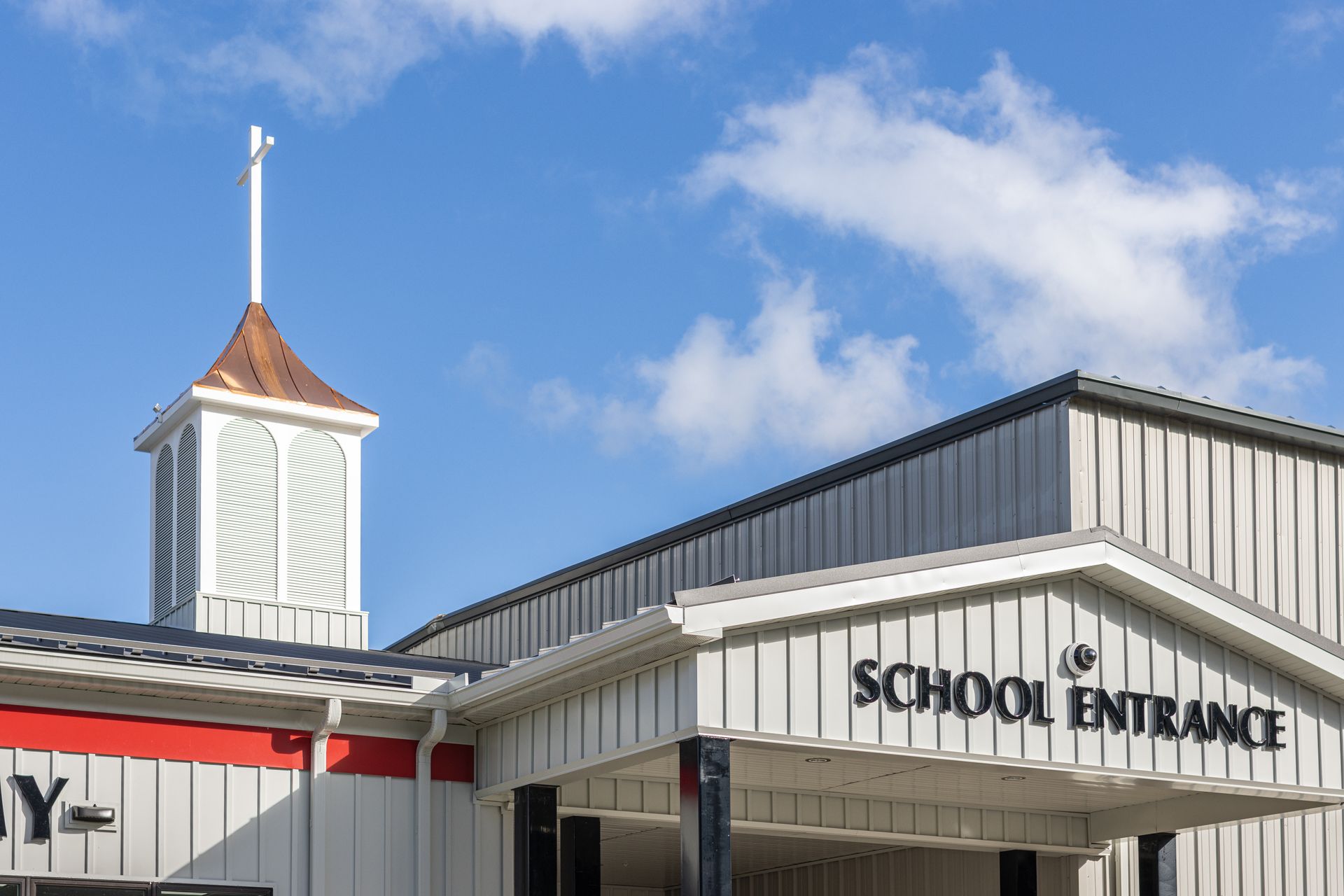 School entrance with a white building, a tower, and a blue sky.