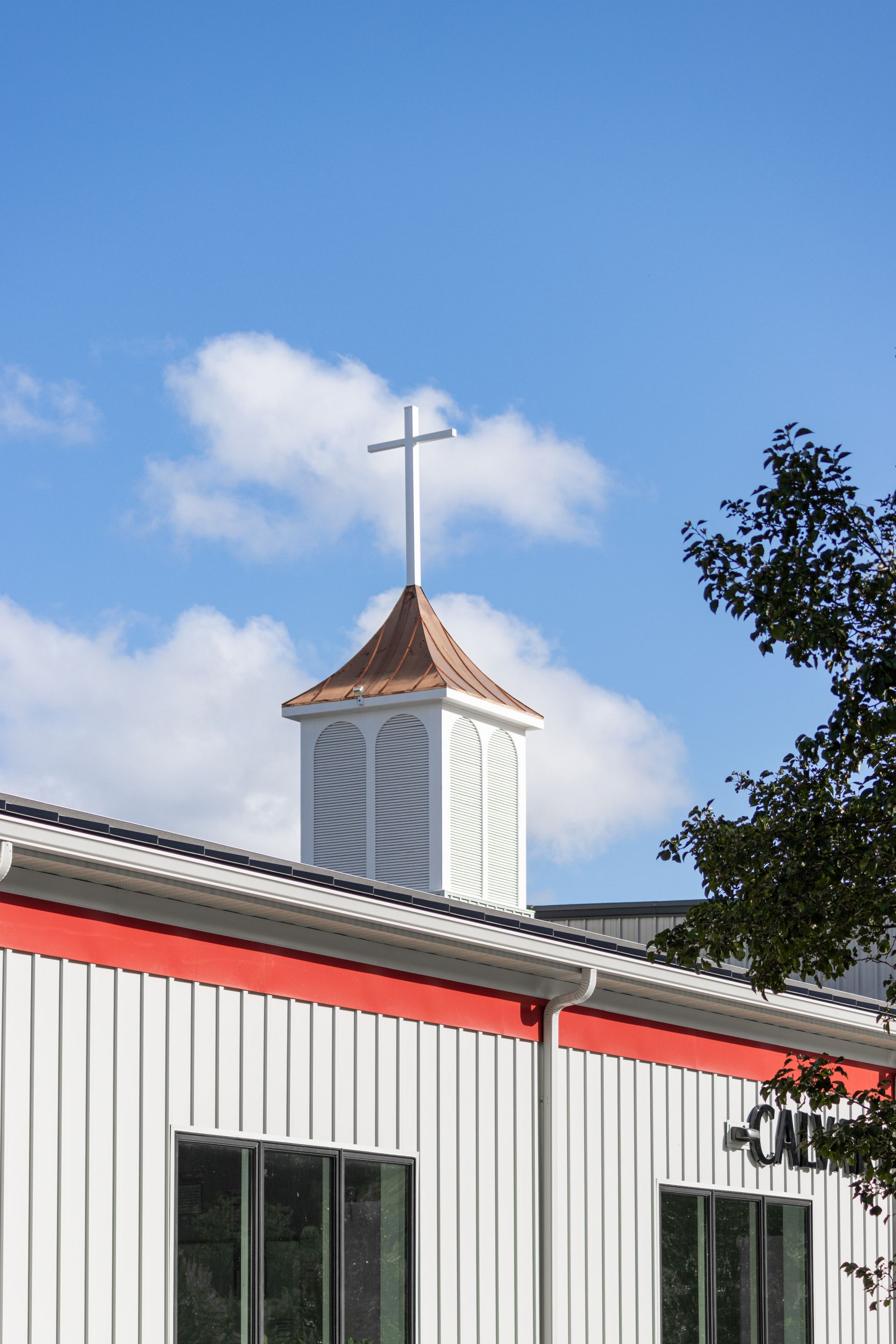 White church building with red trim, steeple, and cross under a blue sky.