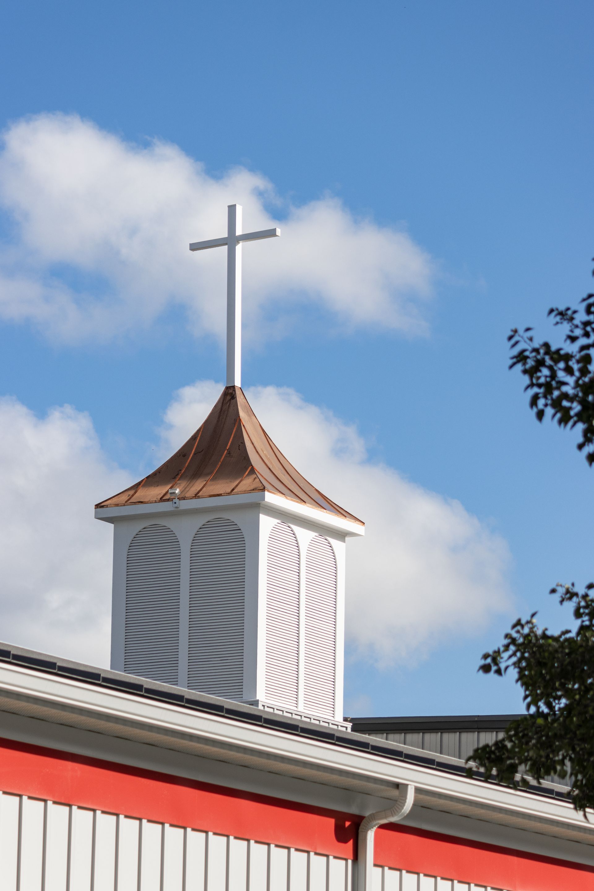 White church steeple with cross against a blue sky. Copper roof.