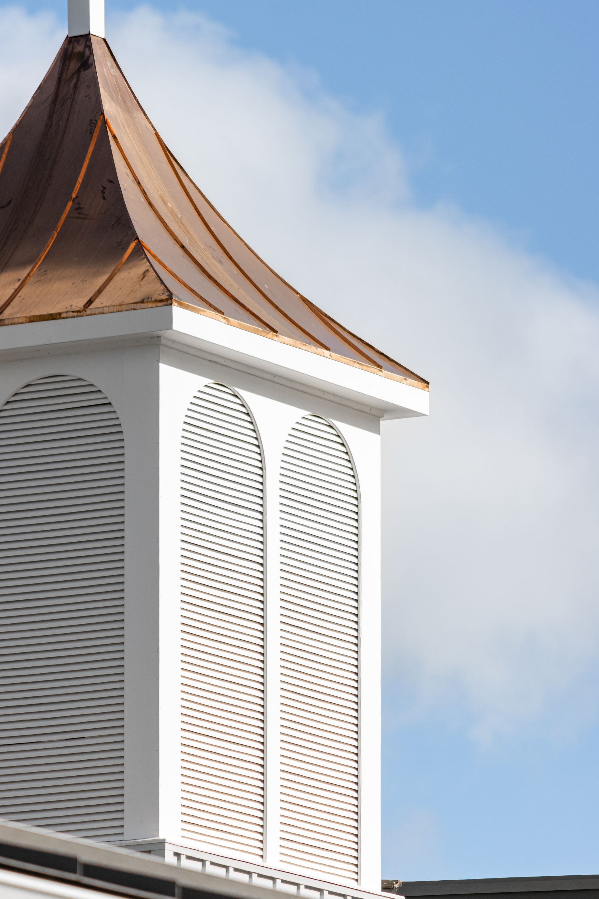 White steeple with copper roof against a blue sky.