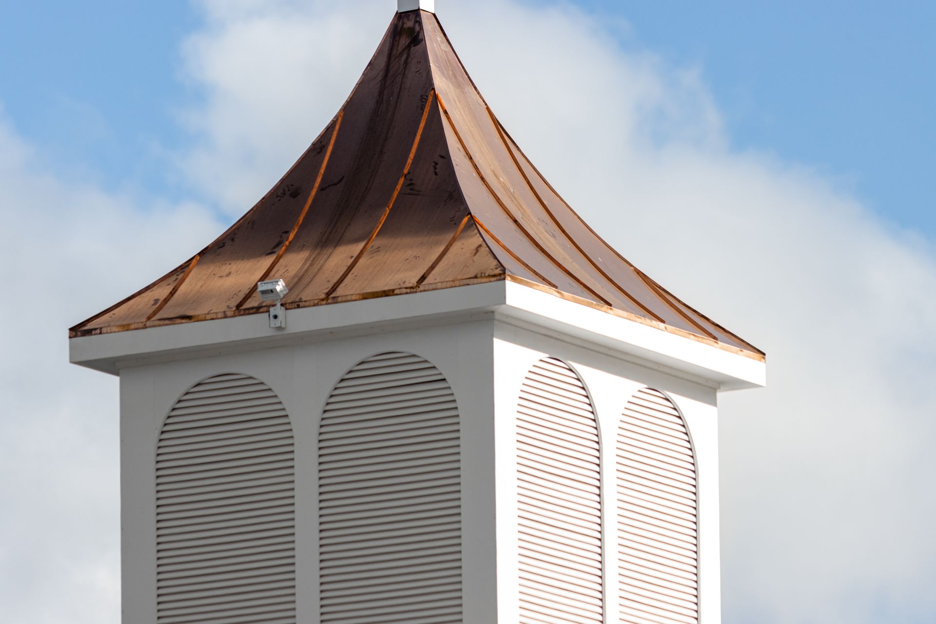 White steeple with copper roof against a blue sky.
