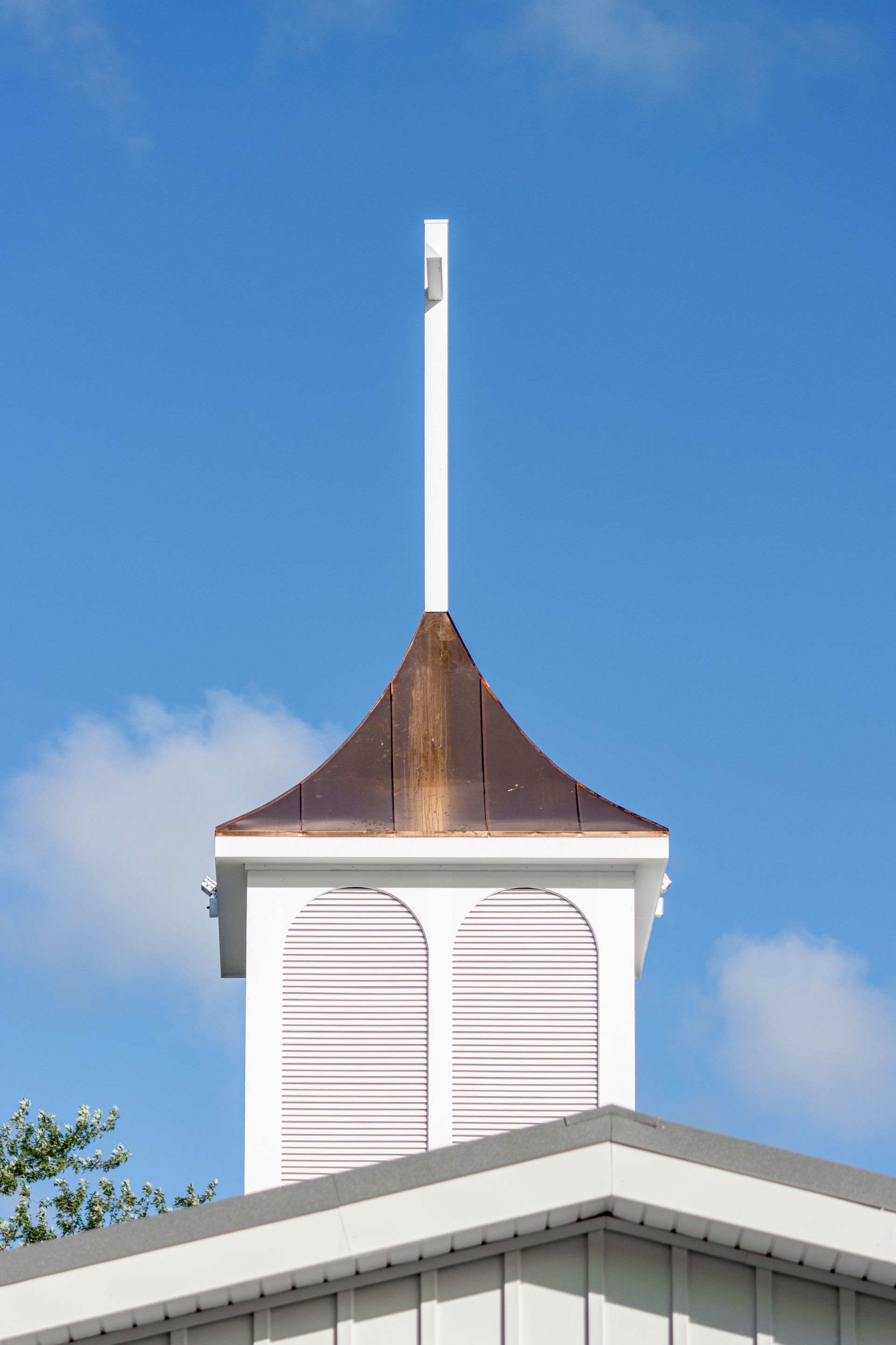 White cupola with copper roof and tall white spire against a blue sky.