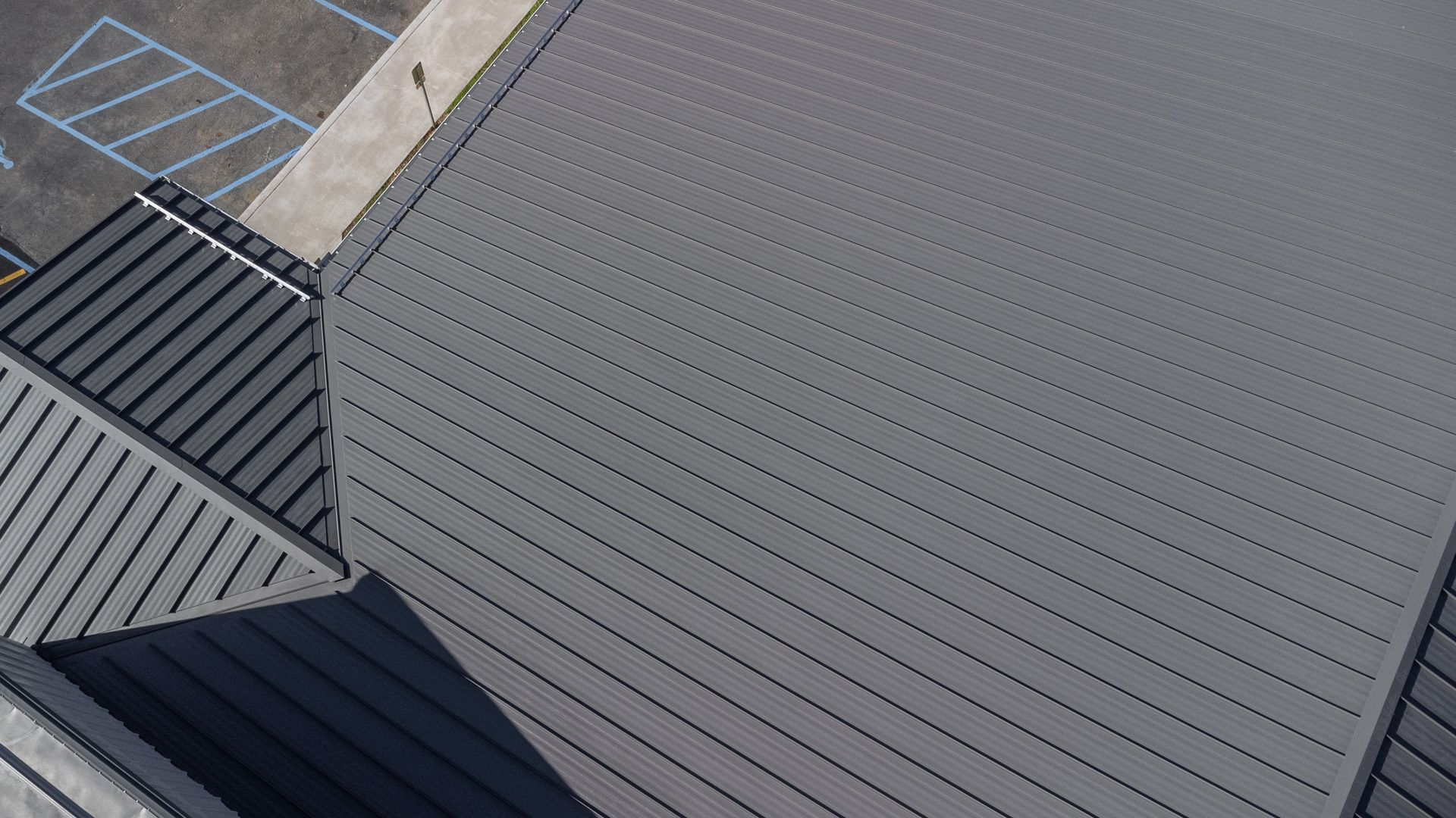 Overhead view of a gray metal roof with angled lines and a section of asphalt.