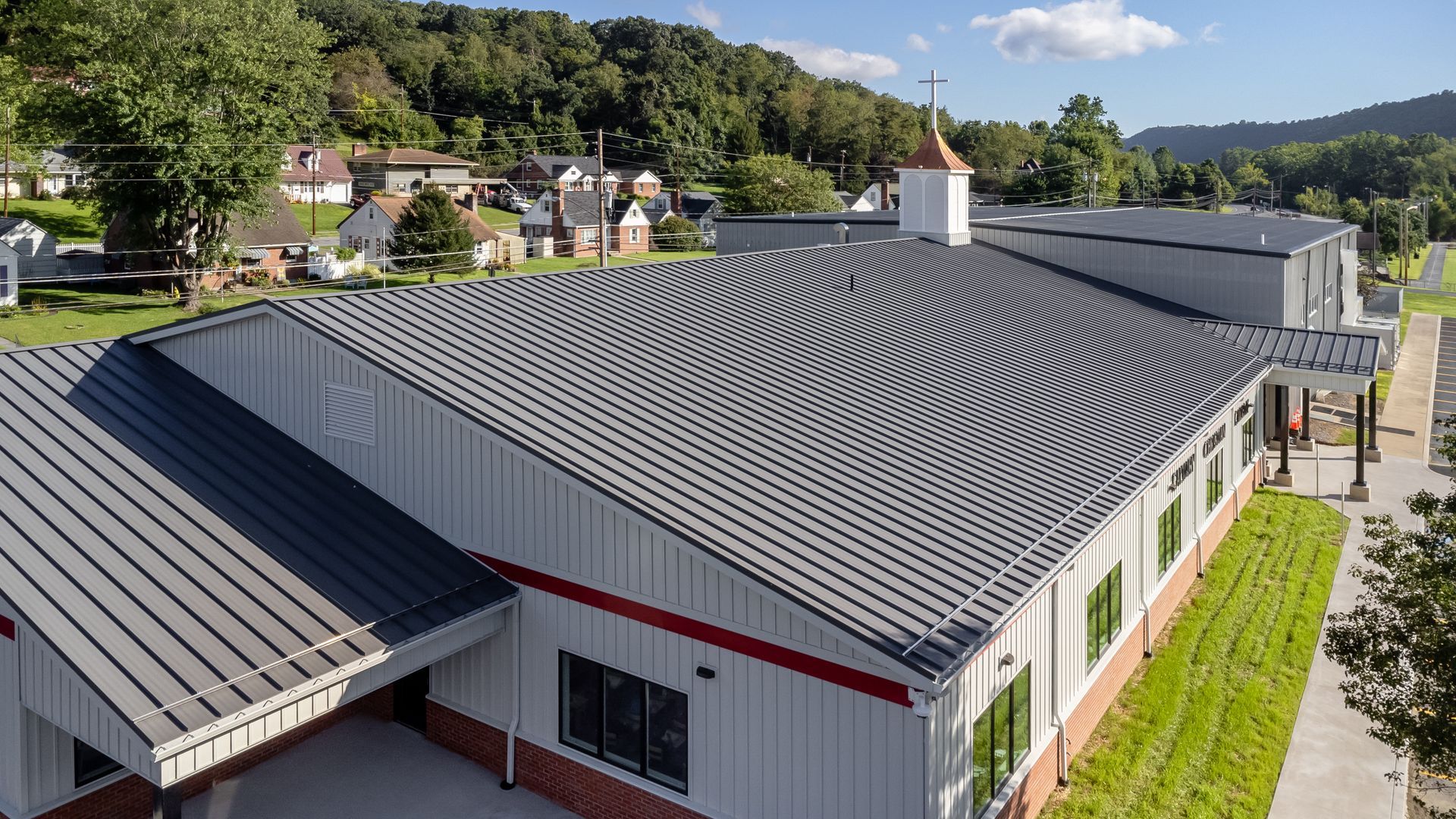 Large metal-roofed building with a red trim and steeple in a town with green hills.